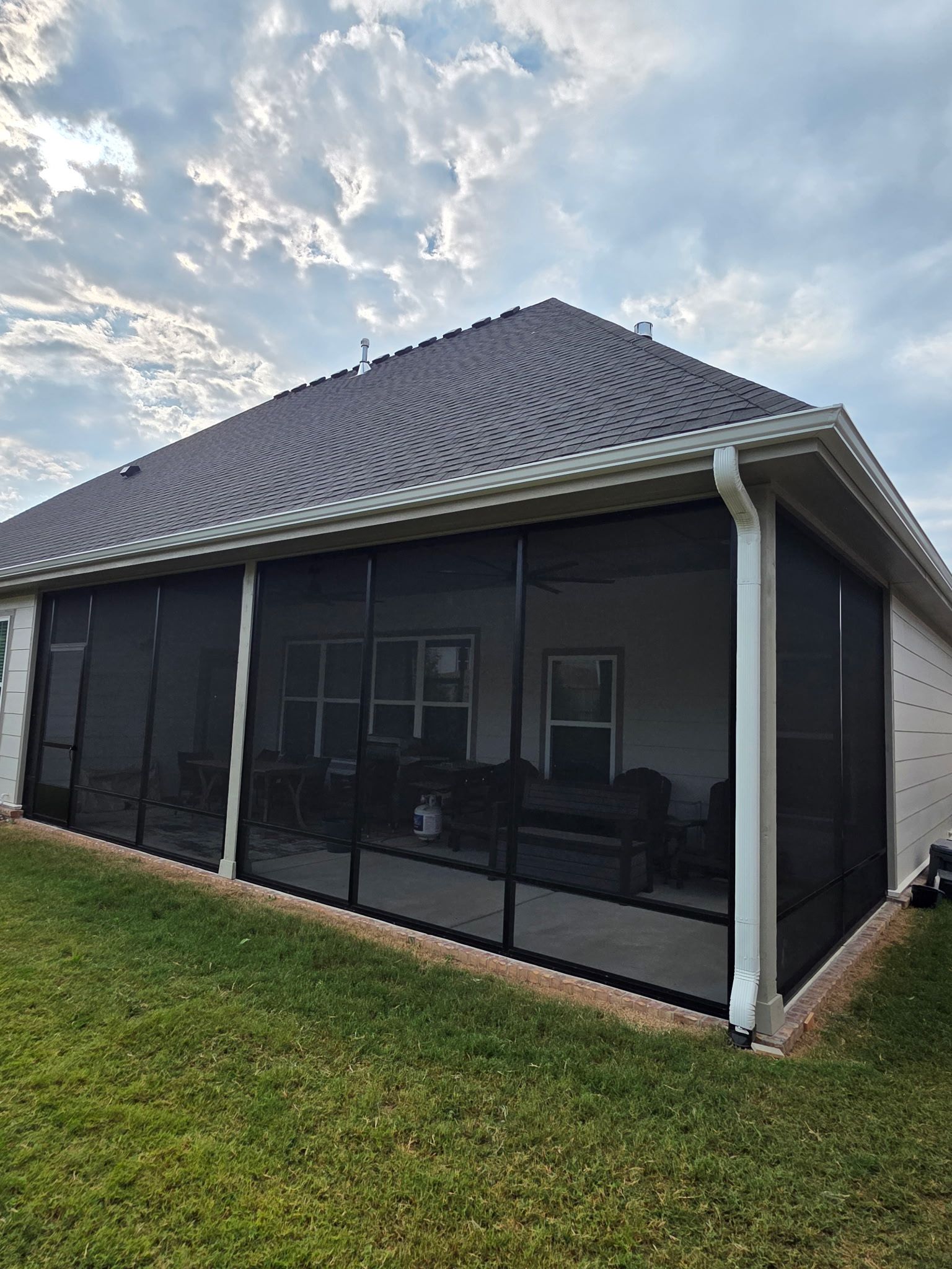 Screened patio on a house with a dark tiled roof and white columns, viewed from the lawn.