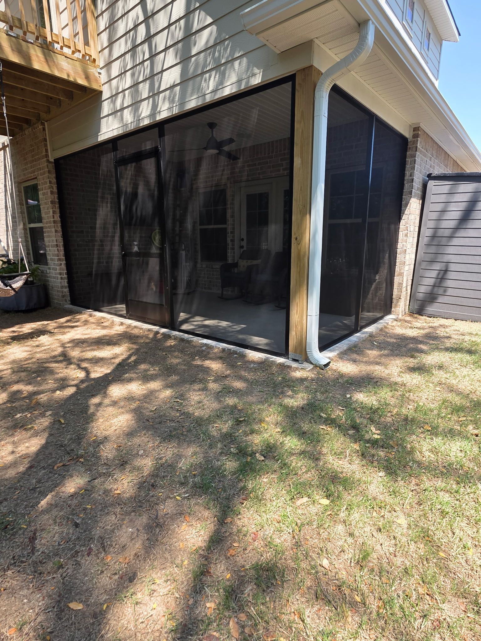 Backyard patio with black mesh screening under a house overhang and a grassy yard.