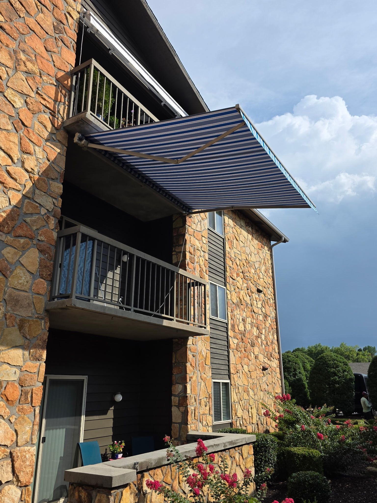 Balcony with striped awning on a stone apartment building under a partly cloudy sky