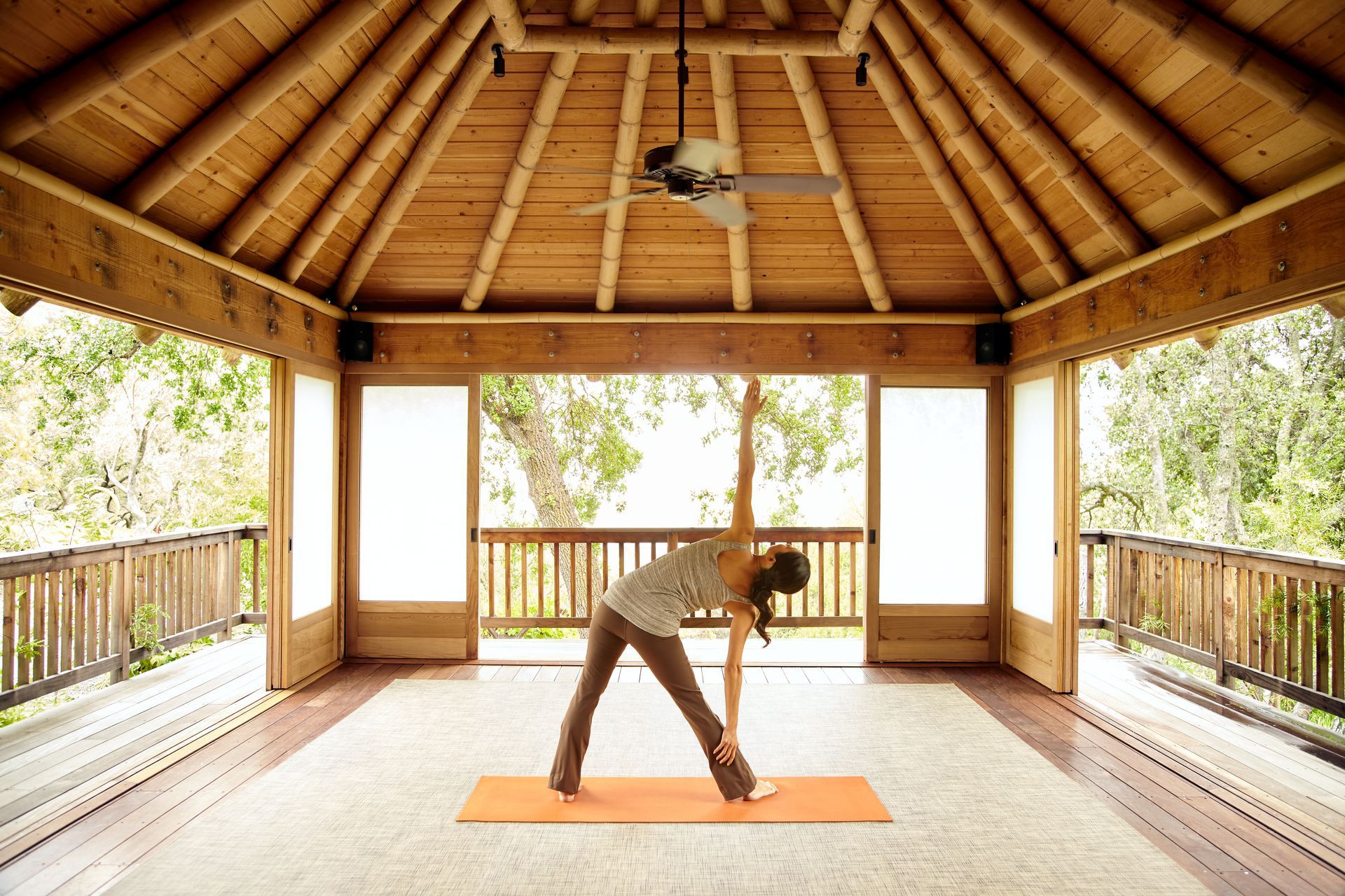 Person stretching on an orange mat in a thatched-roof open pavilion.