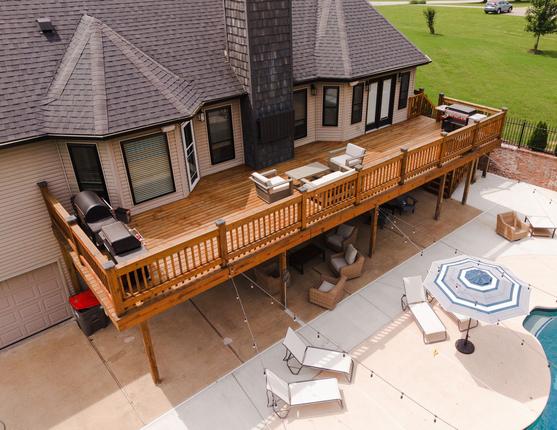 Raised wooden deck with grill and patio furniture beside a house and backyard pool