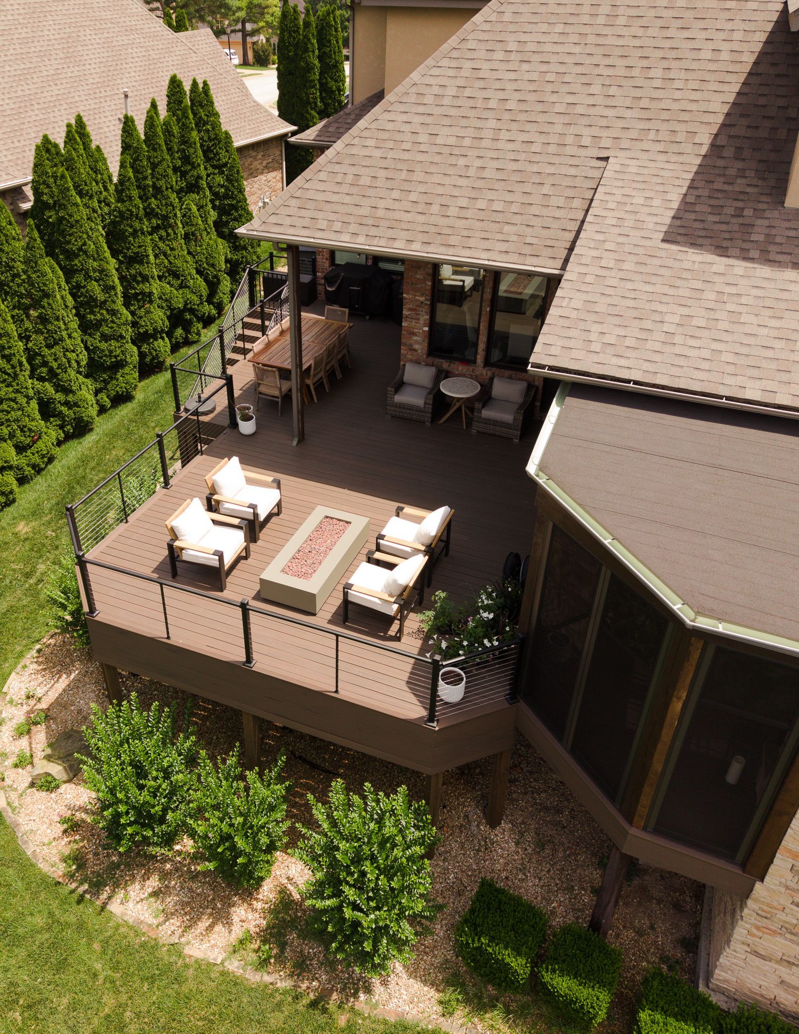 Patio deck with white outdoor furniture beside a tan house and tall green hedges