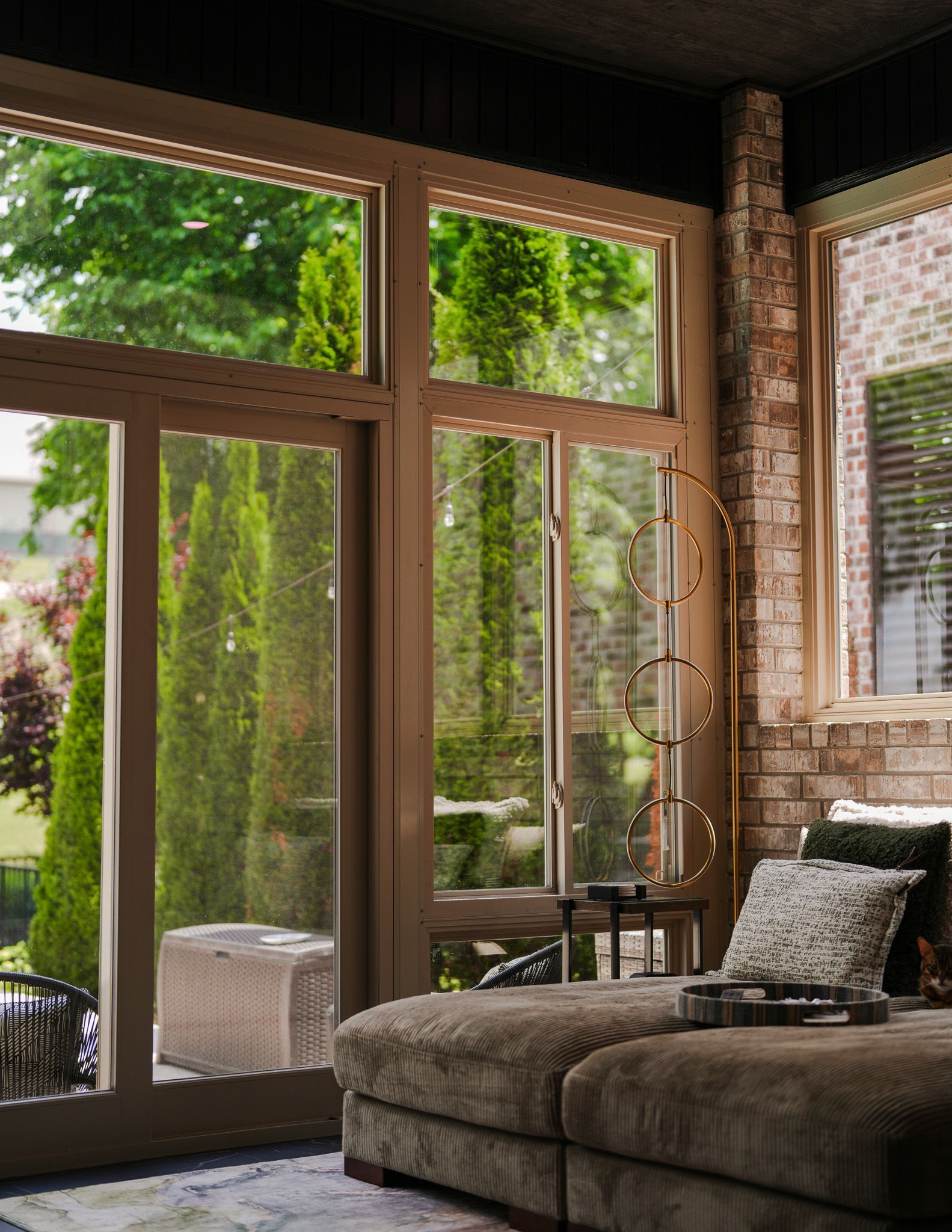 Cozy sunlit living room with large glass doors, a sectional sofa, and greenery outside.