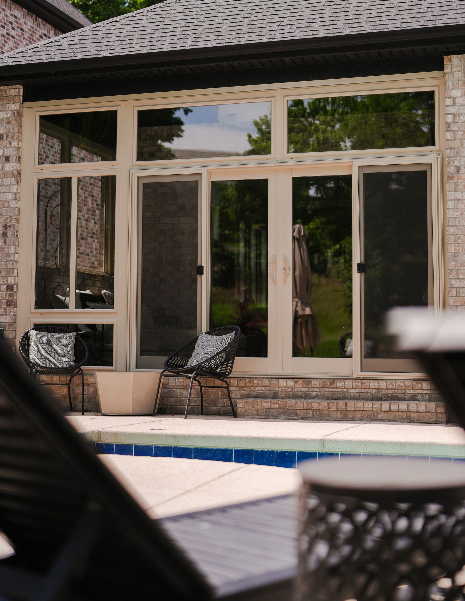 Patio with a swimming pool, stone house exterior, and glass French doors under a covered roof.