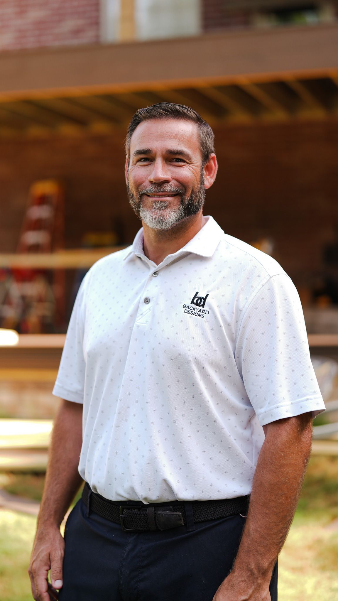Smiling man in a green striped polo shirt with arms crossed against a plain wall.