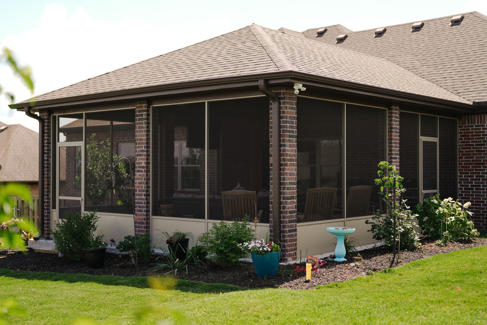 Single-story brick house with screened patio, beige roof, and landscaped yard