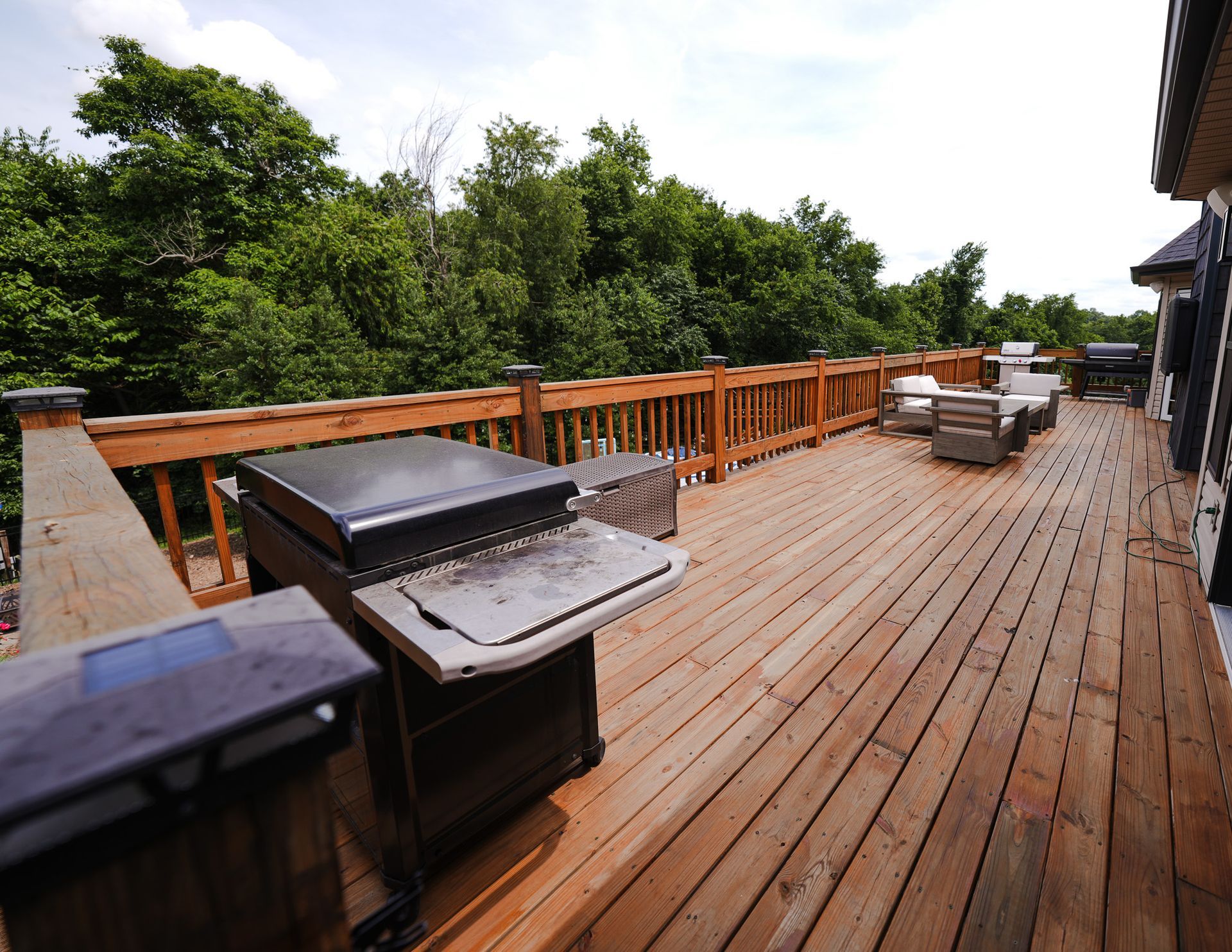 Wooden deck patio with grill and outdoor seating overlooking lush green trees