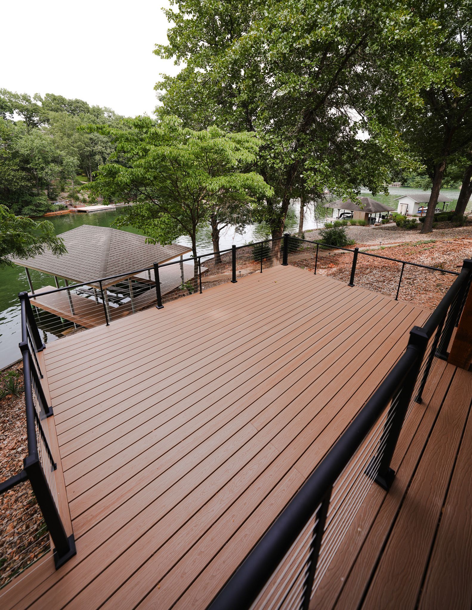 Wooden deck with black railings overlooking trees and a waterfront path
