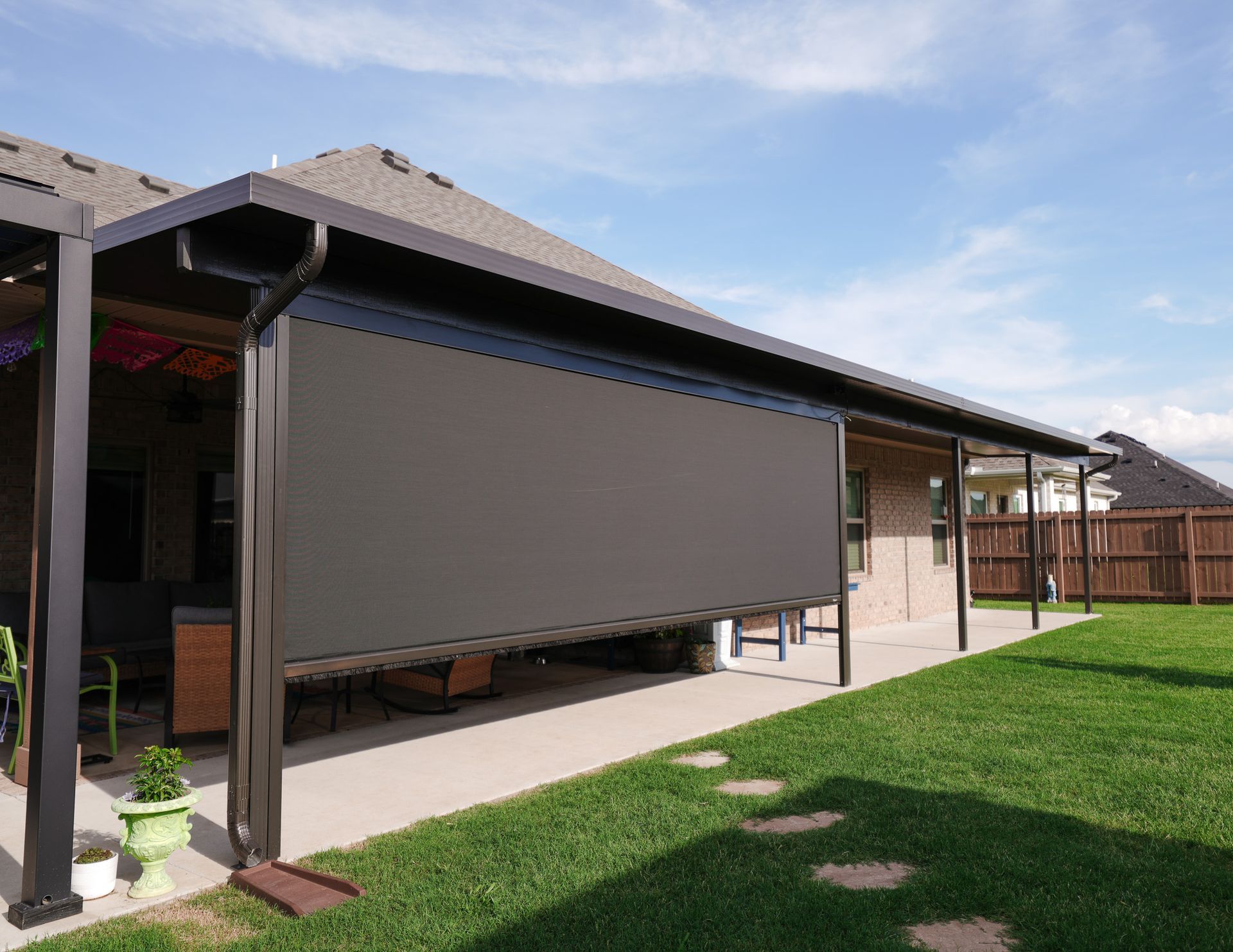 Backyard patio with retractable gray awning, lawn, and wooden fence under a blue sky