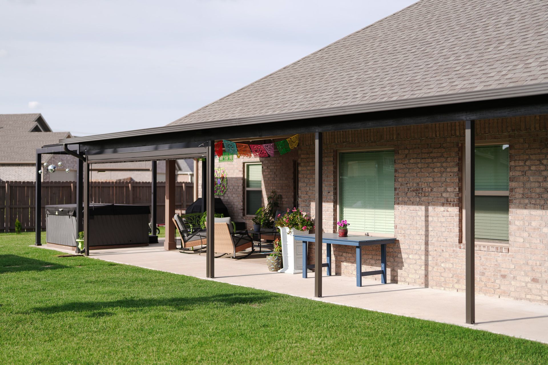 Back patio with covered seating, grill, and lawn beside a brick house
