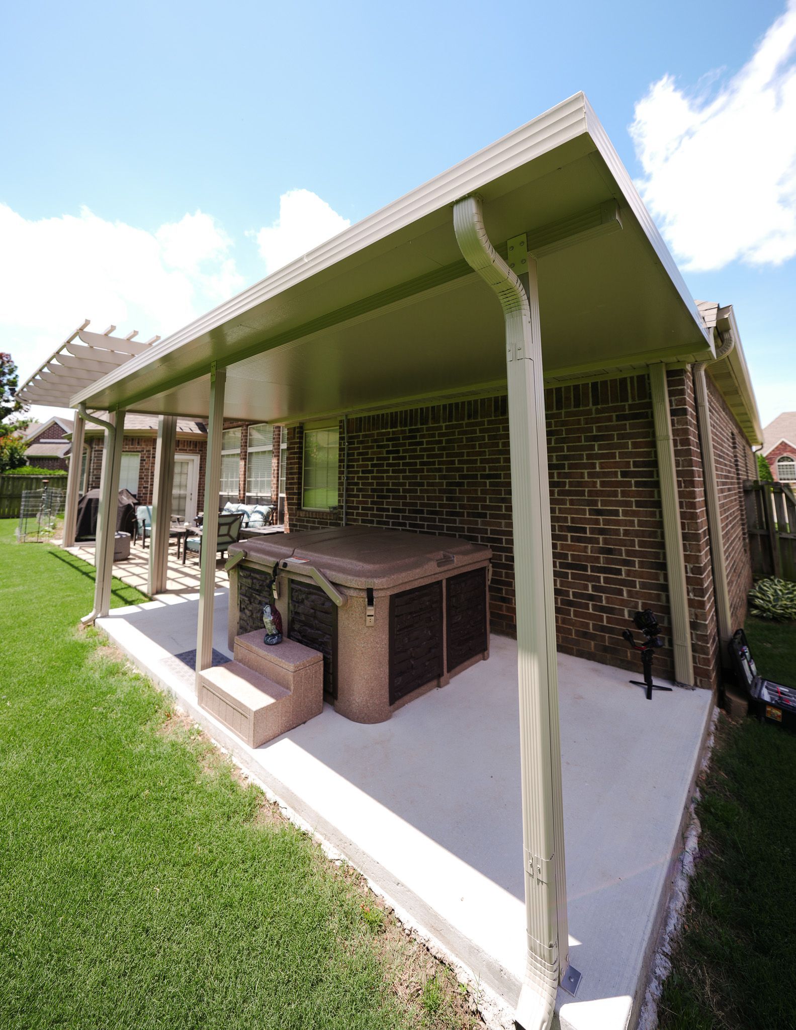 Outdoor covered patio with a grill, brick wall, and green lawn under a bright sky