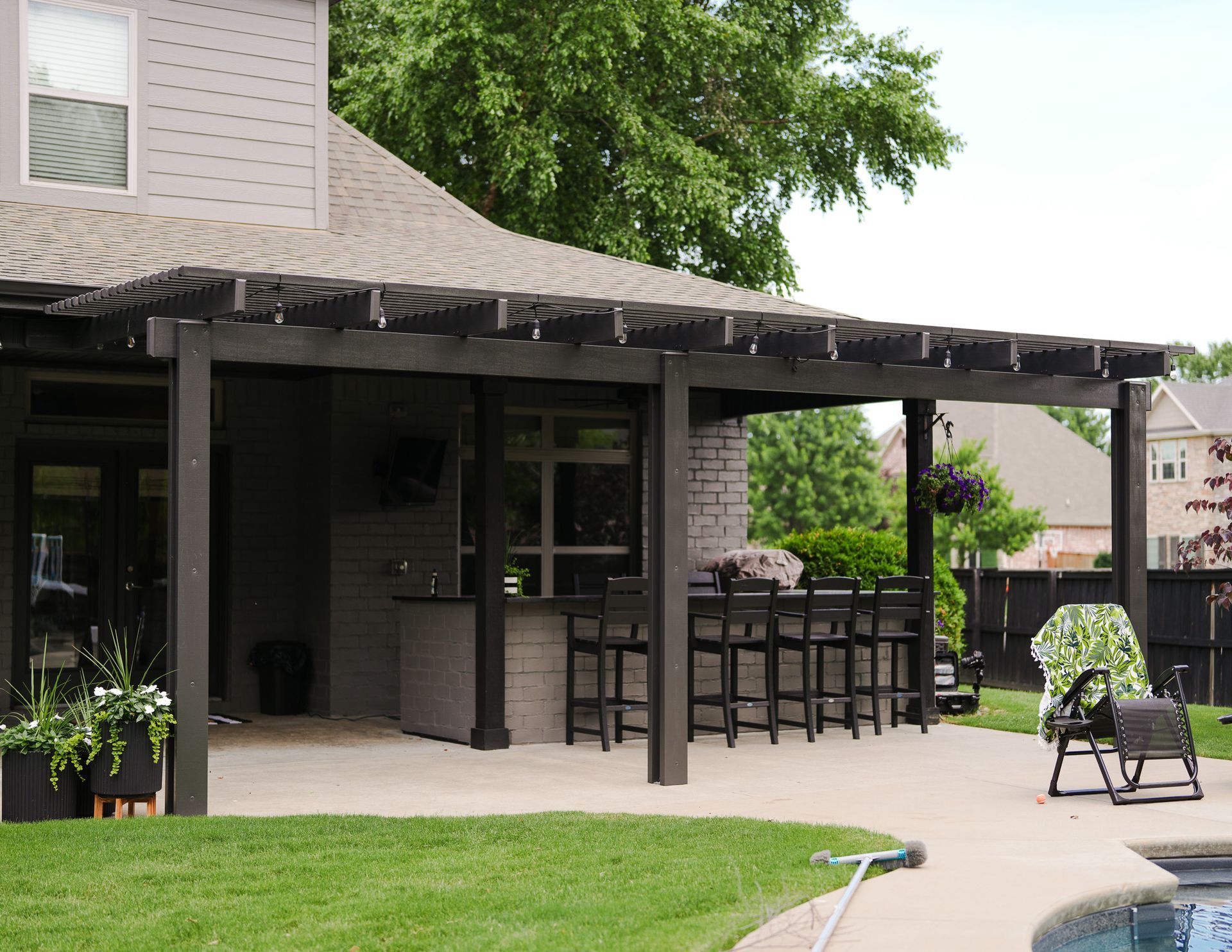 Backyard patio with covered pergola, bar seating, and a swimming pool beside a house