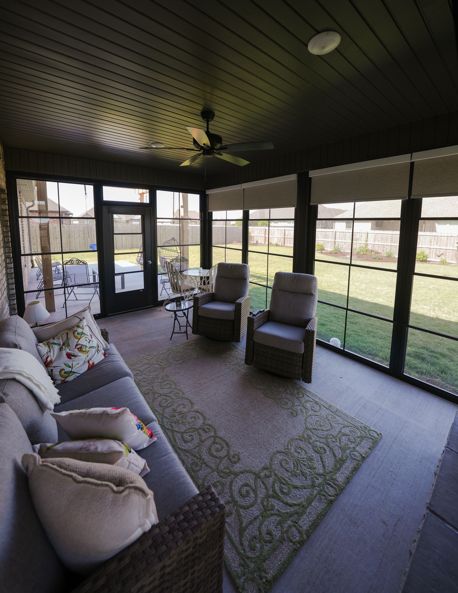 Covered patio seating area with sofa, chairs, and rug overlooking a fenced backyard.