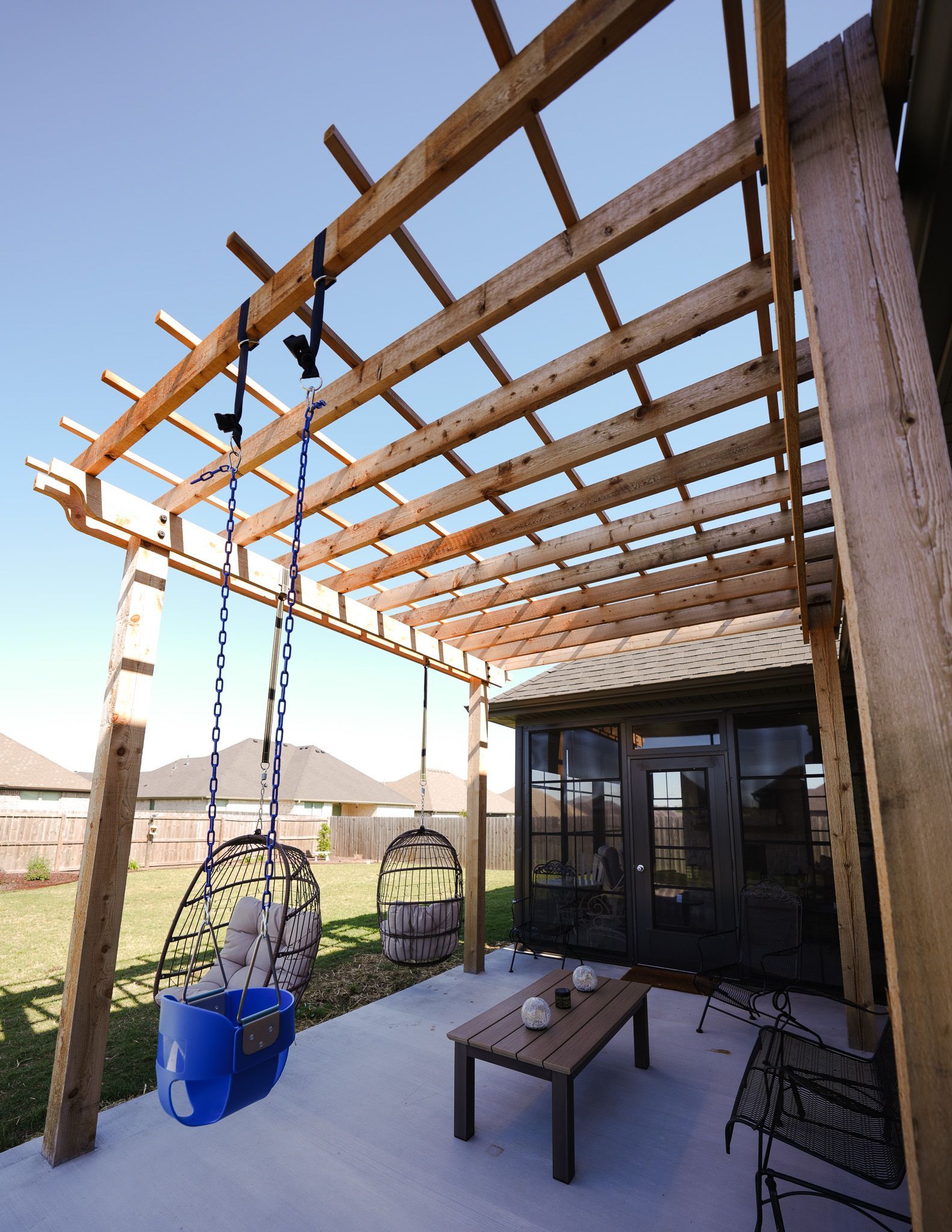 Patio with wooden pergola, hanging lanterns, table, chairs, and a view of open fields