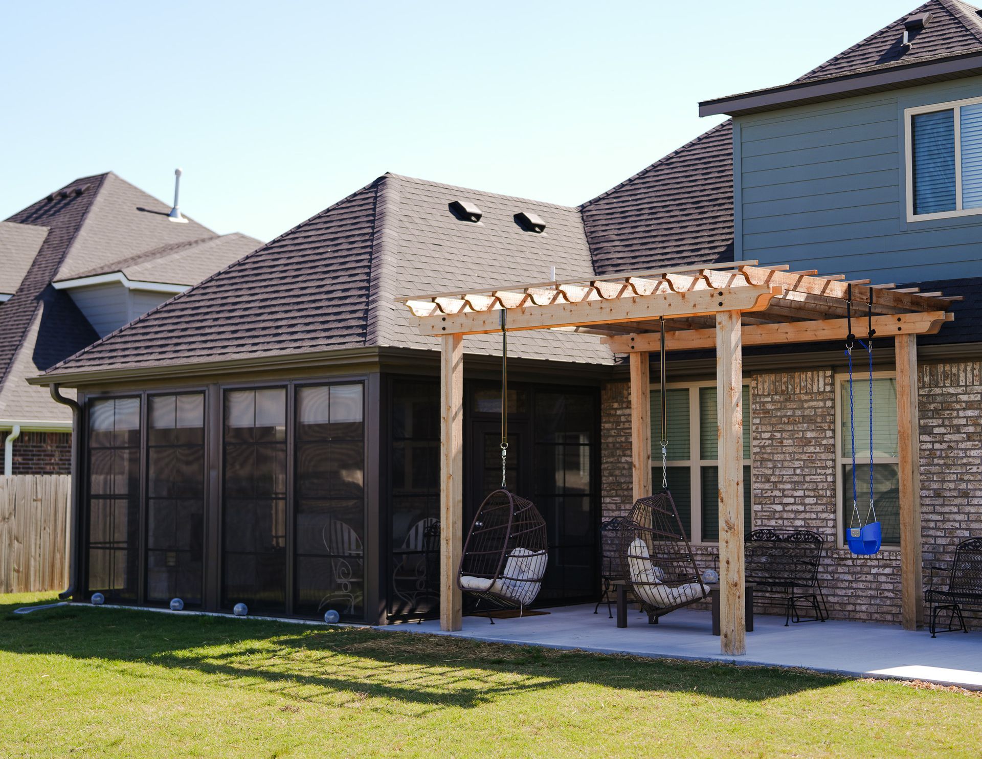 Backyard patio with pergola, screened porch, and brick house exterior under a clear sky
