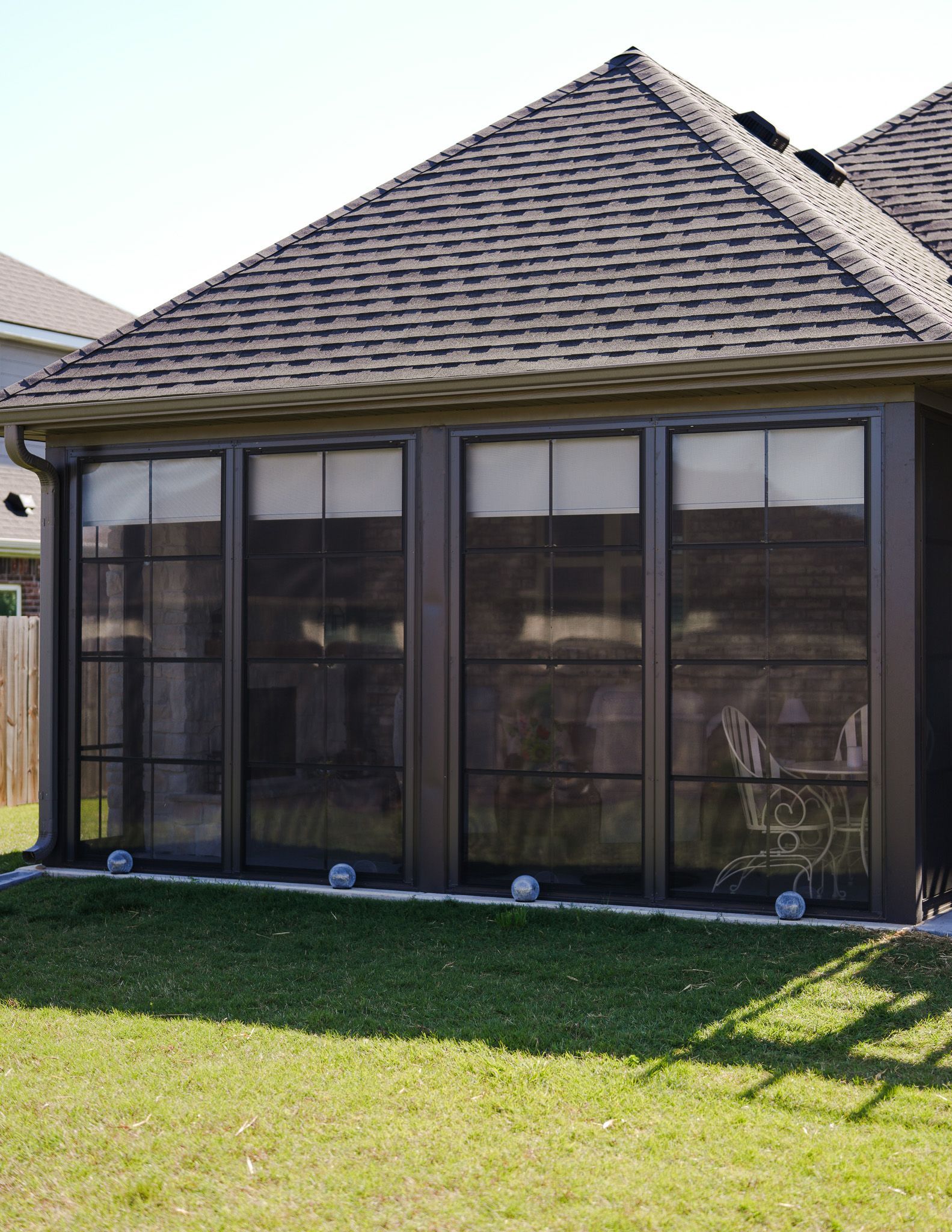 Screened patio with dark mesh windows beneath a shingled roof beside a grassy yard