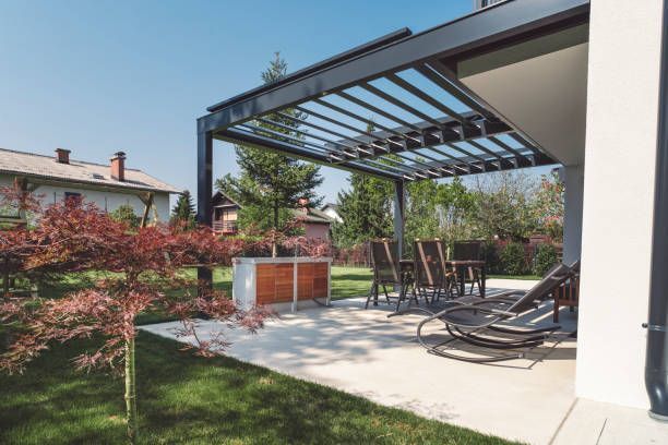 Modern patio with pergola, outdoor dining table, and lounge chairs beside a lawn and garden