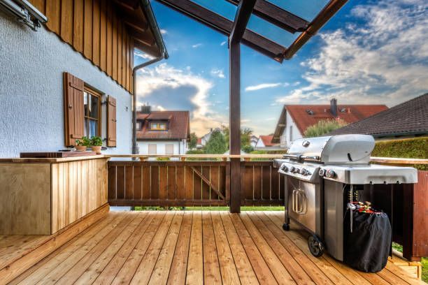 Wooden deck with a stainless grill, overlooking houses under a partly cloudy sky