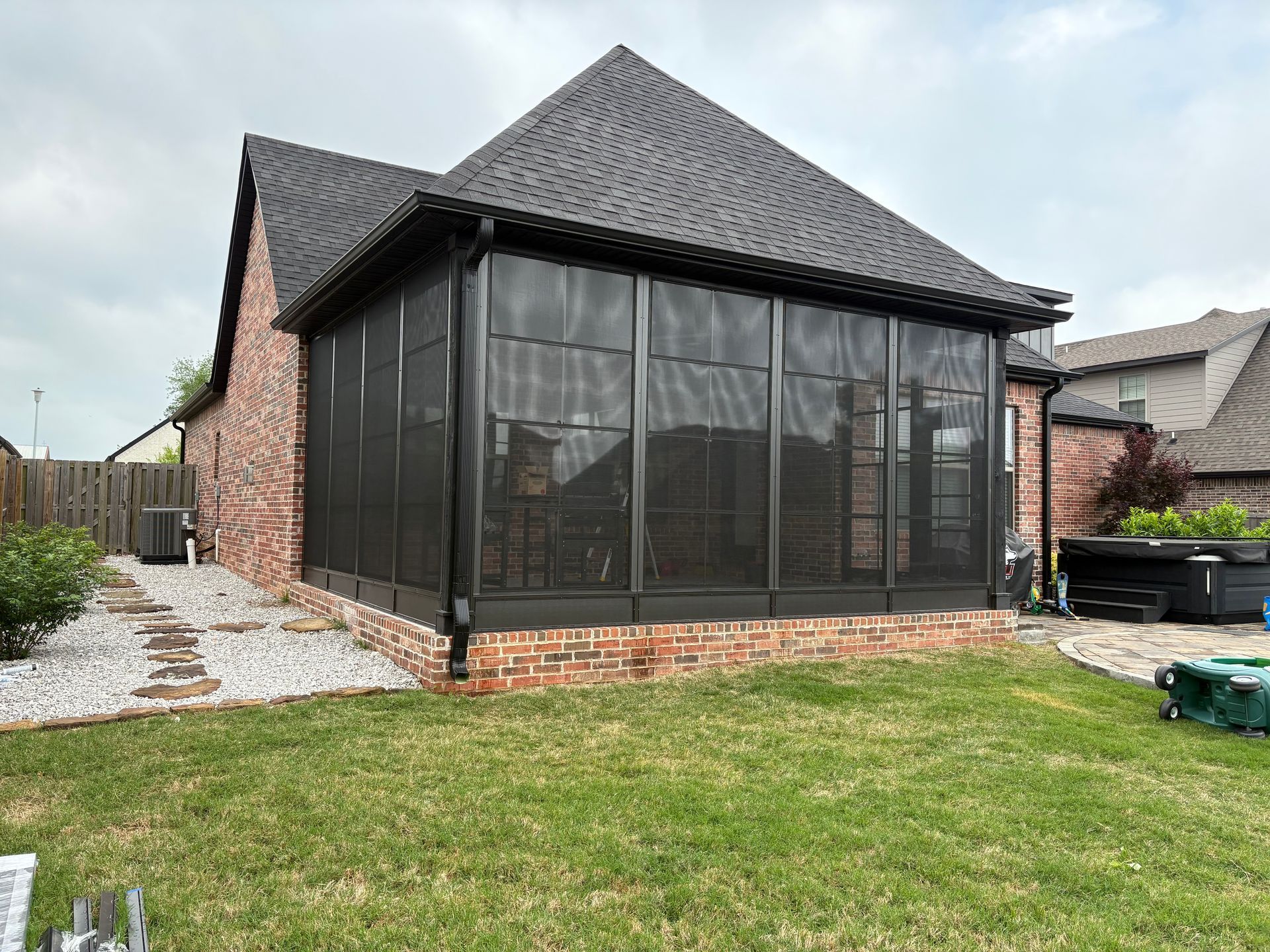 Brick sunroom with dark screened windows and a gray roof in a grassy backyard