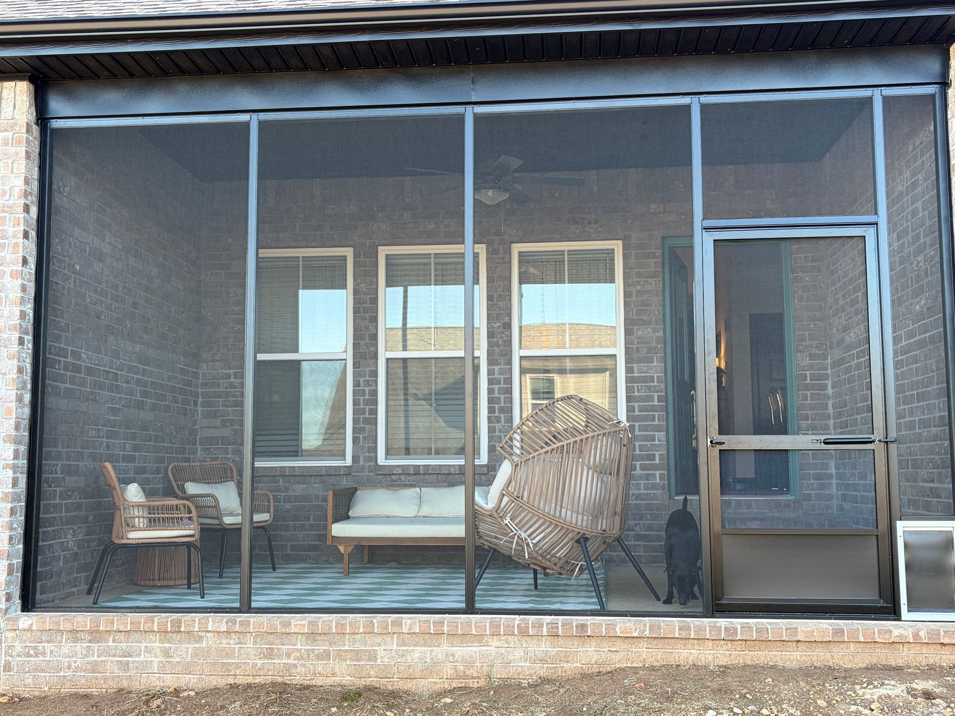 Screened patio with wicker chairs, a bench, and glass sliding doors on a brick house