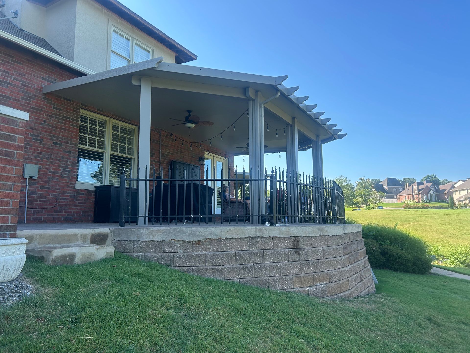 Brick house porch with black railing on a grassy slope under a clear blue sky