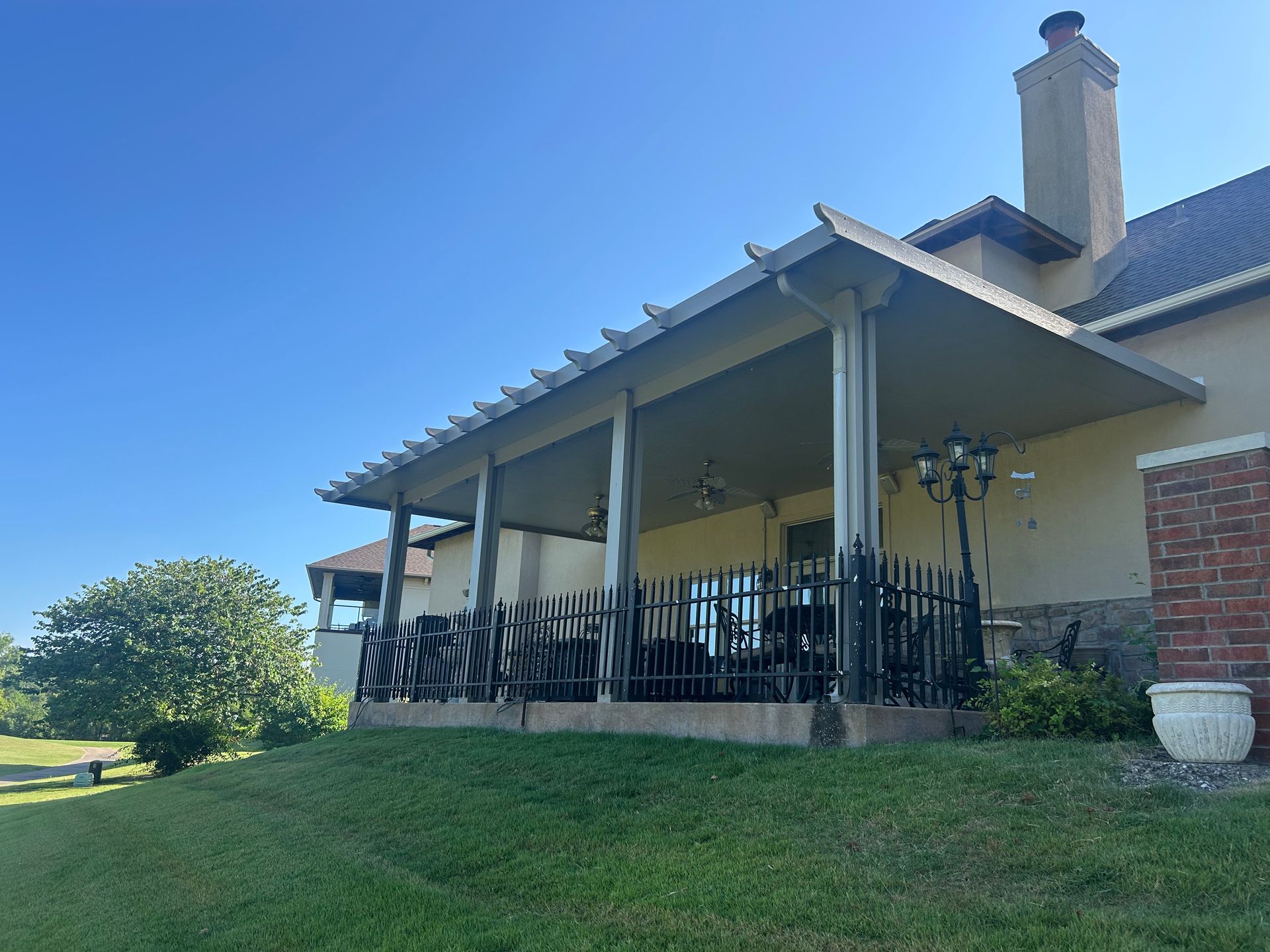 House with porch, black railing, brick chimney, and grassy lawn under a clear blue sky