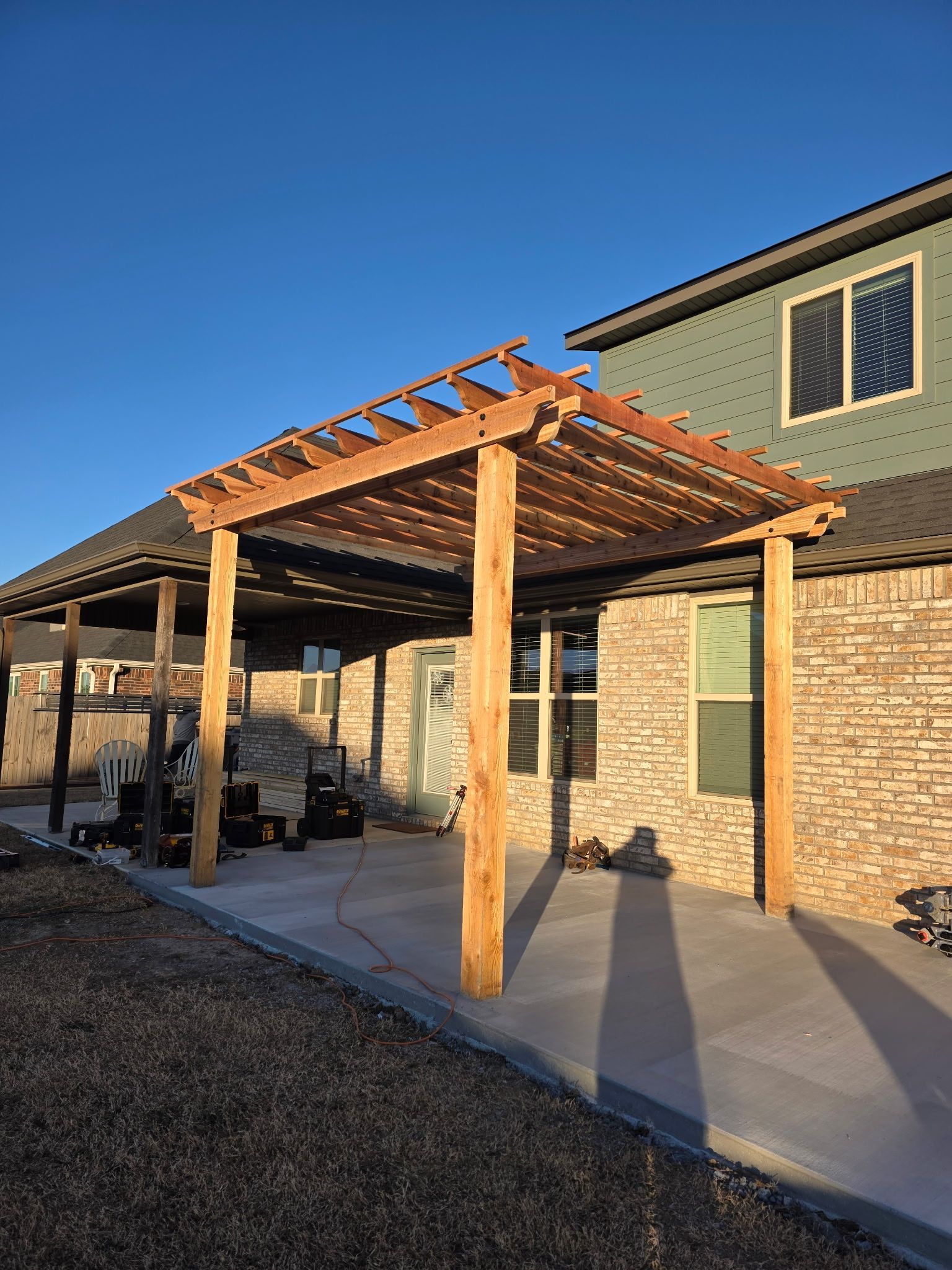 Back patio with a wooden pergola over a concrete slab beside a brick house at sunset