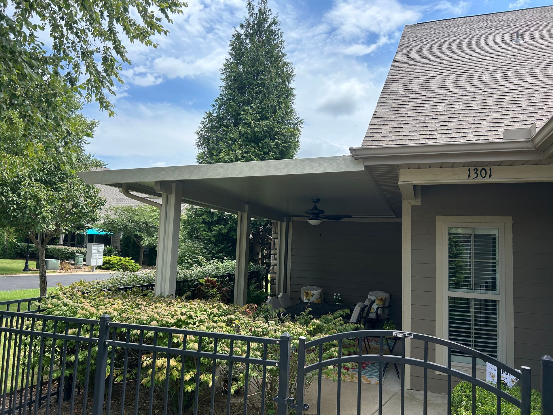 Front porch with black metal fence, beige house facade, and trees under a partly cloudy sky