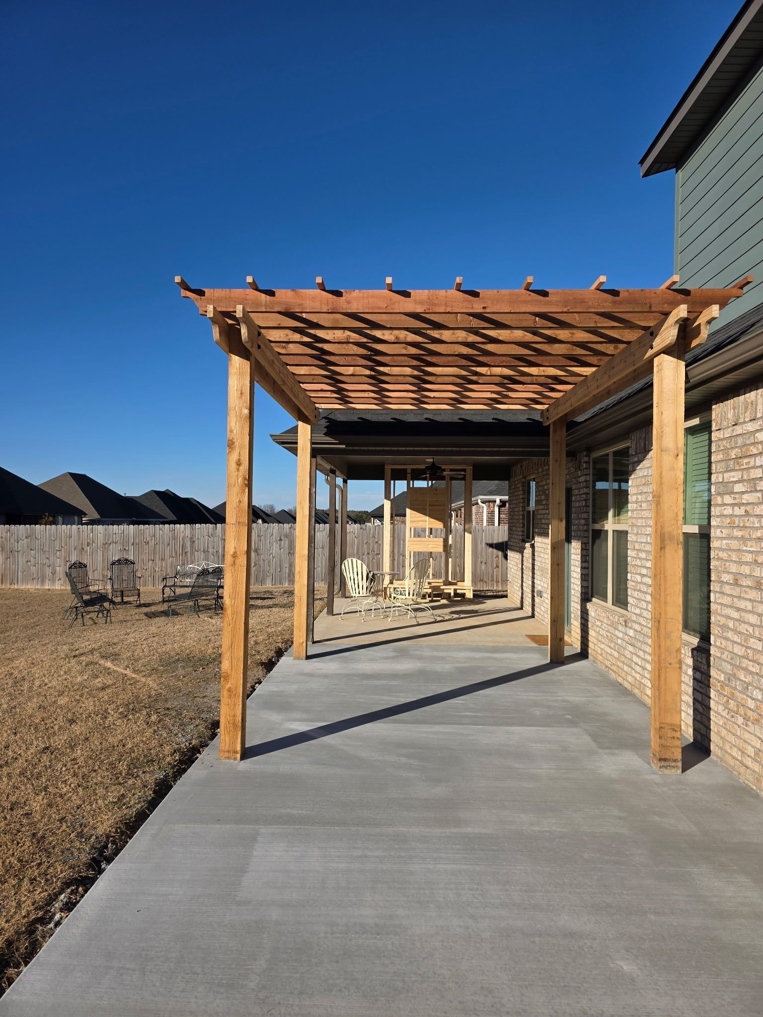 Covered concrete walkway with wooden pergola beside a brick building under a clear blue sky