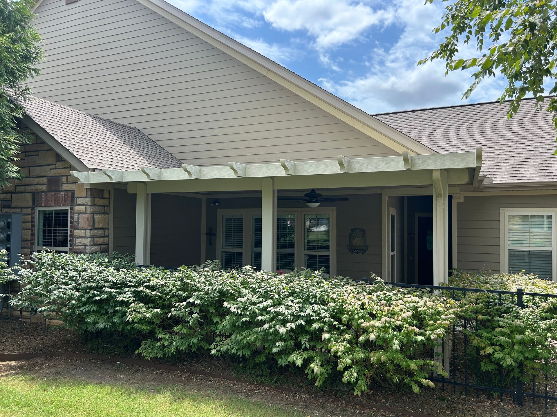 Suburban house with a covered porch, white siding, and dense flowering shrubs in front
