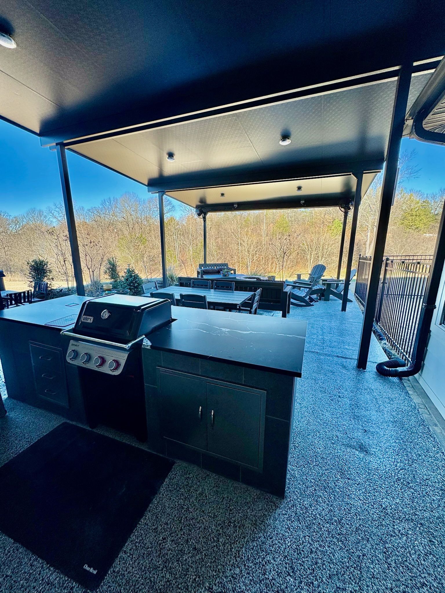 Covered outdoor patio with black grill, dining table, and chairs overlooking trees and mountains