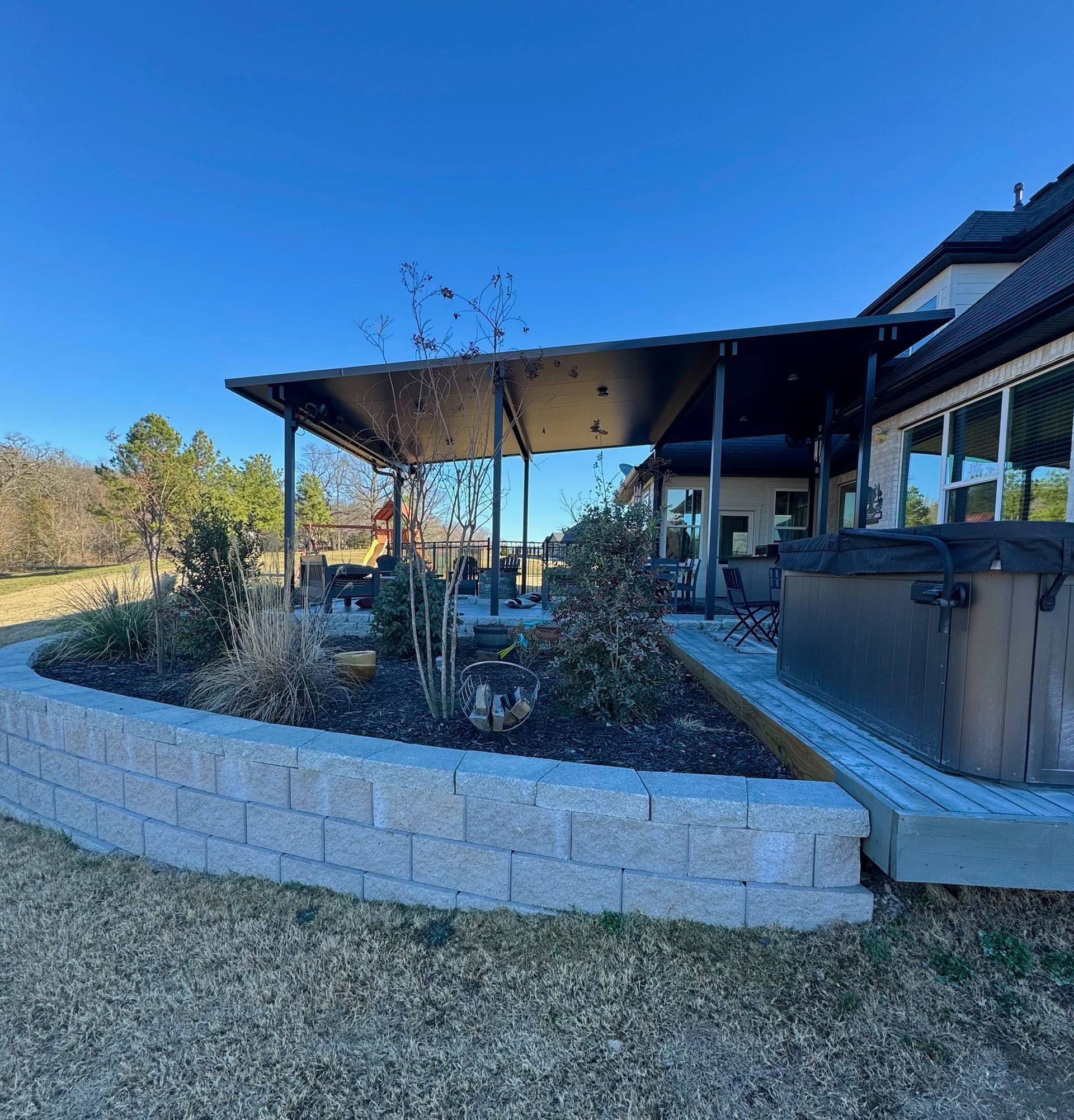 Modern house patio with raised stone garden beds and a covered outdoor seating area under a blue sky