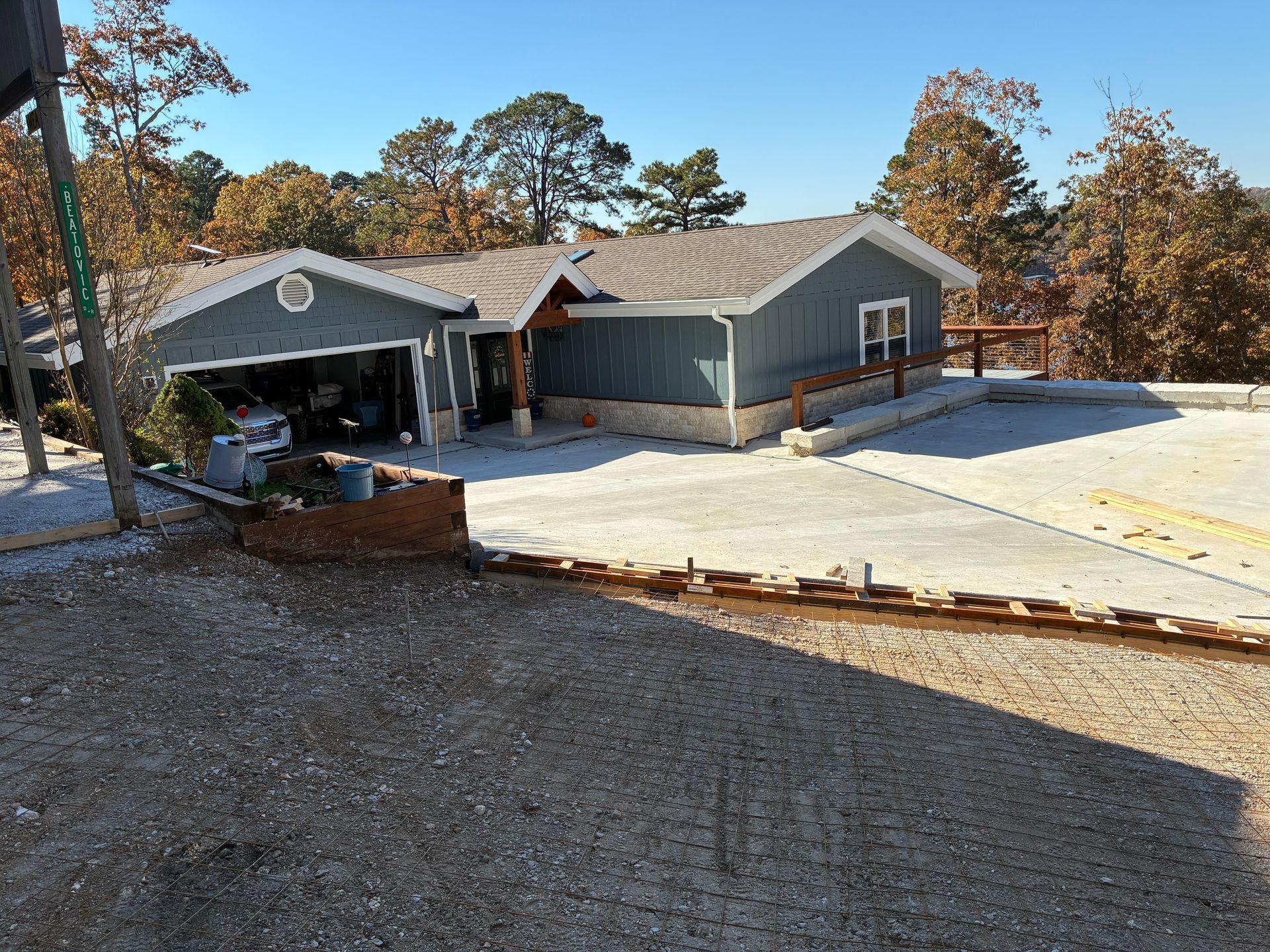 Driveway and garage of a gray house in a wooded suburban neighborhood on a sunny day