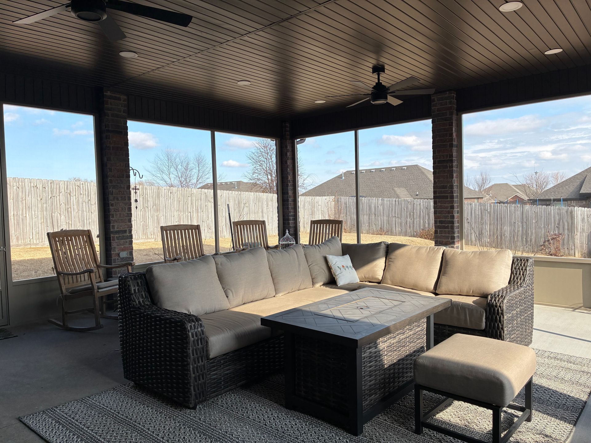 Covered patio with wicker sectional sofa, coffee table, and mountain view through screened openings