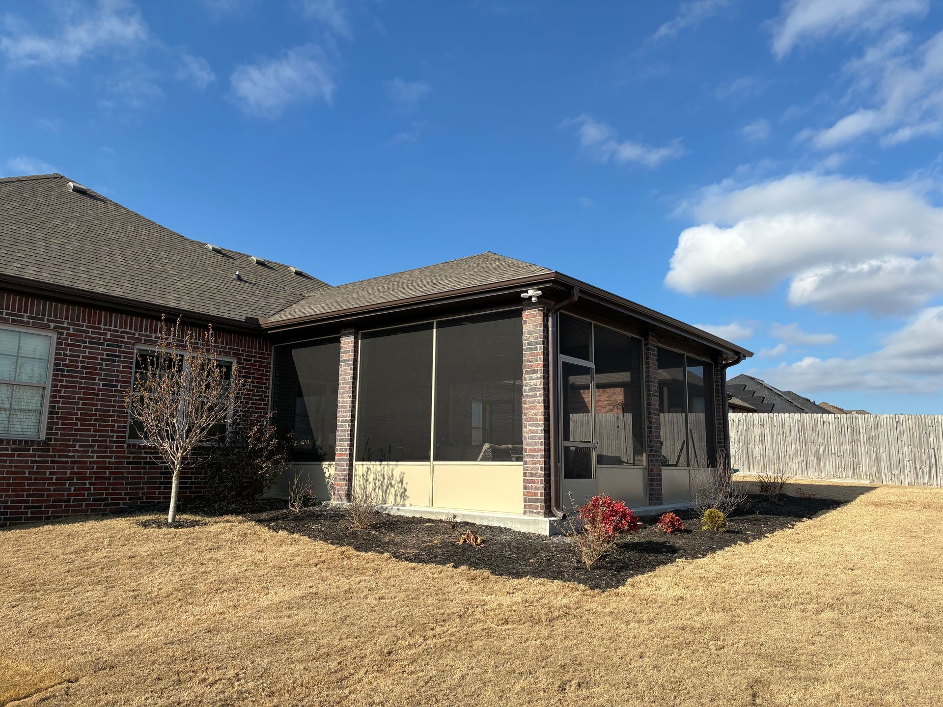 Suburban house with screened patio, brown roof, and dry yard under a blue sky