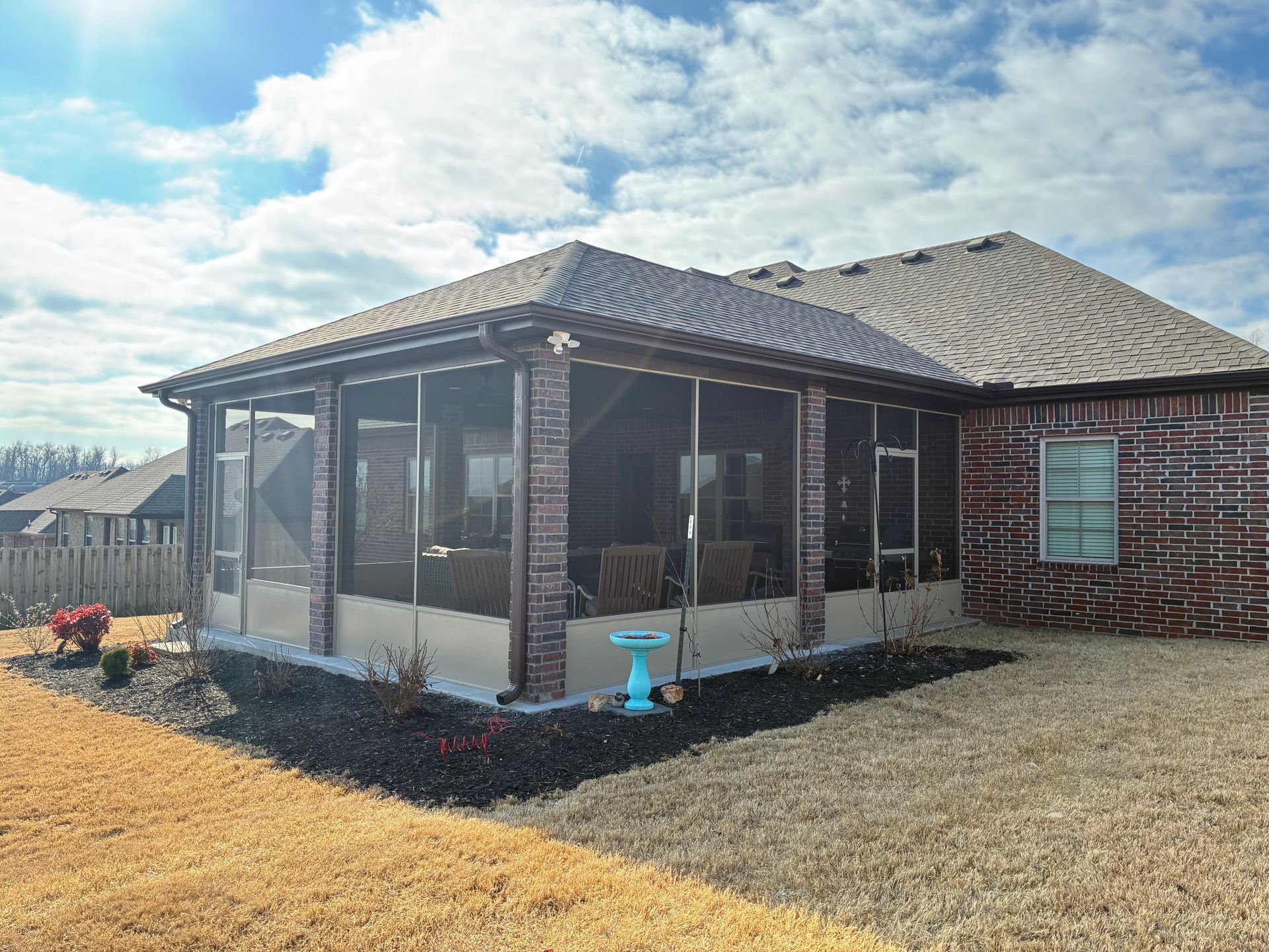 Screened porch attached to a brick house in a dry suburban yard under a cloudy sky