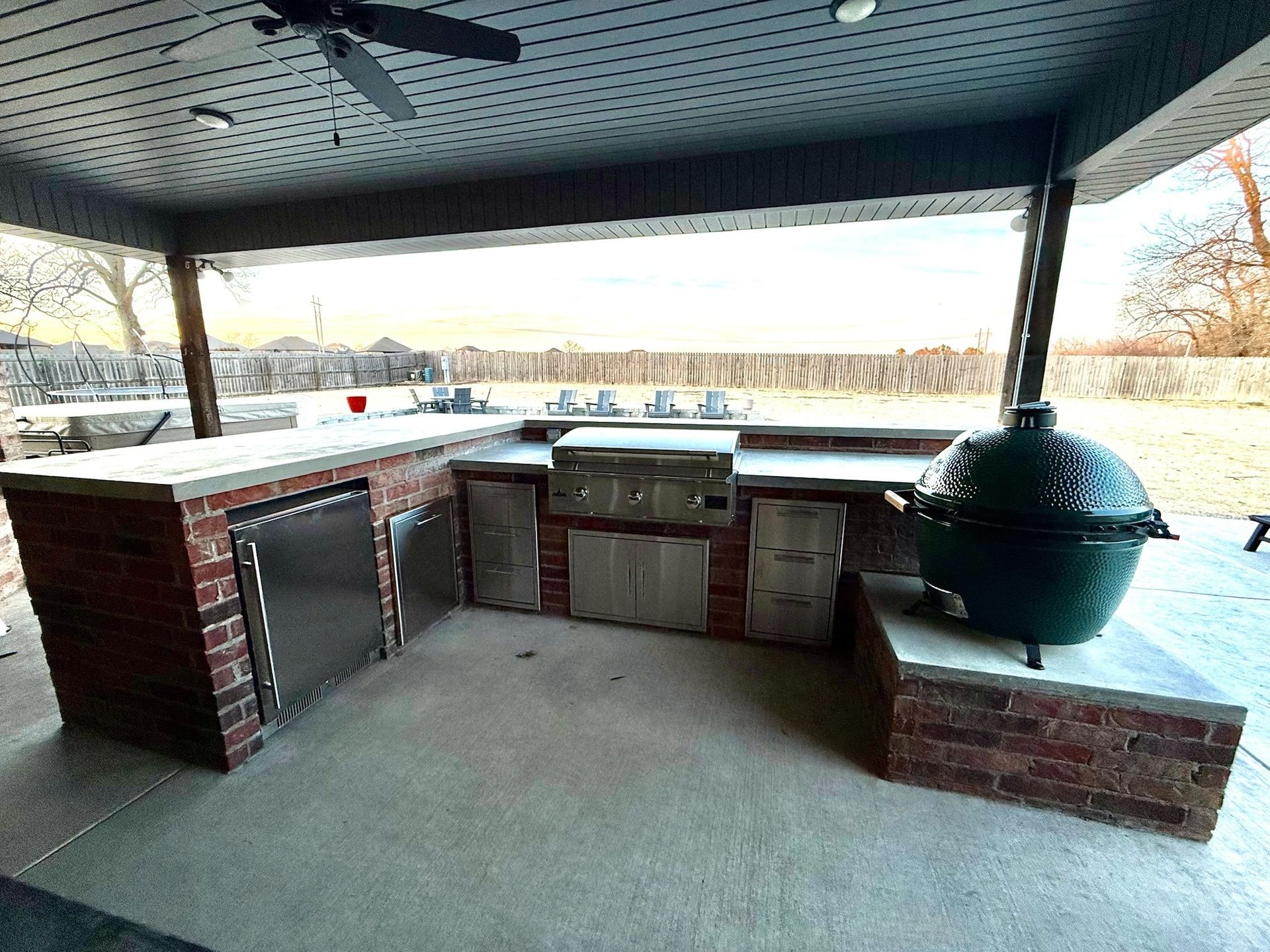 Outdoor brick patio with built-in grill, sink, and green kamado smoker under a covered roof