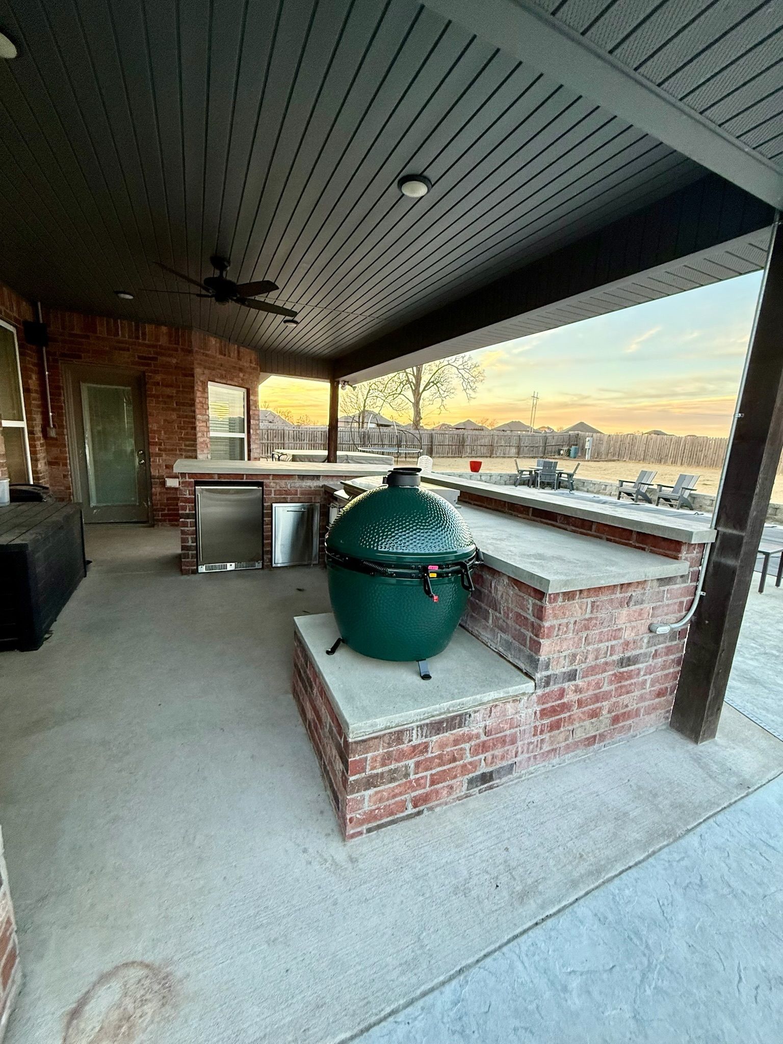 Covered brick patio with a green ceramic grill/smoker overlooking a sunset skyline.