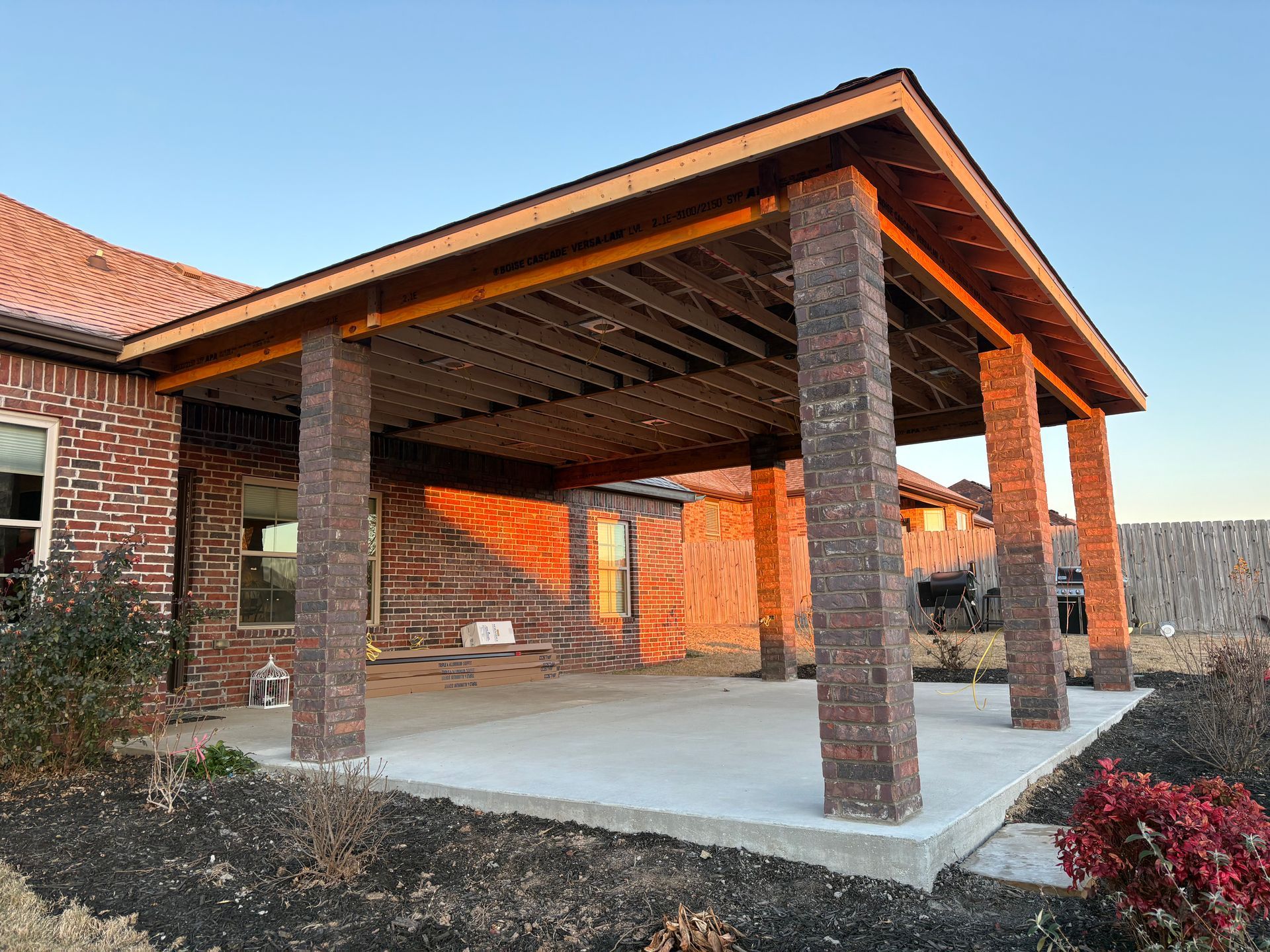 Covered brick patio with four stone columns and a concrete slab beside a brick house