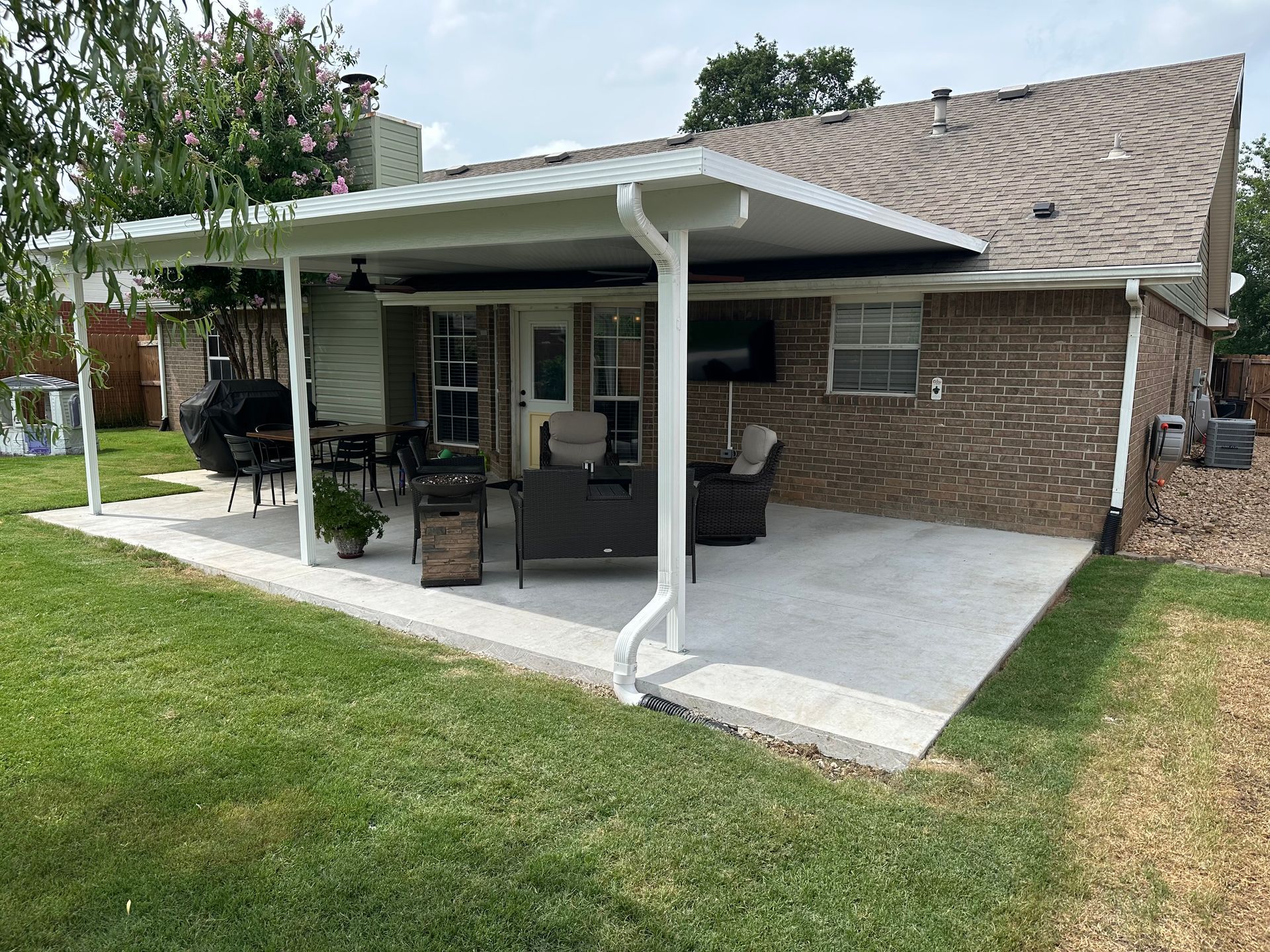 Covered patio with patio furniture beside a brick house and green lawn