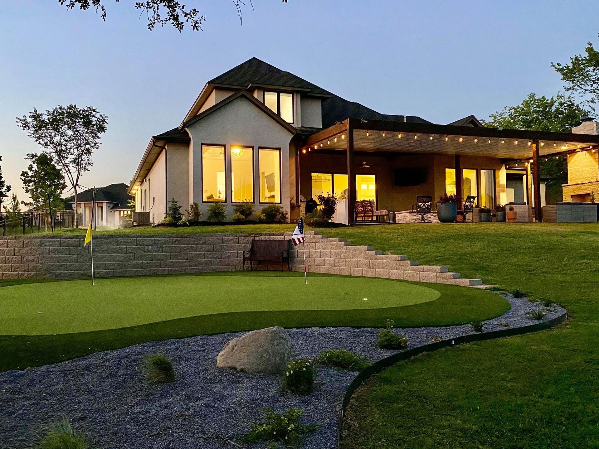 Modern house at dusk with lit windows, covered patio, and landscaped lawn and stone path