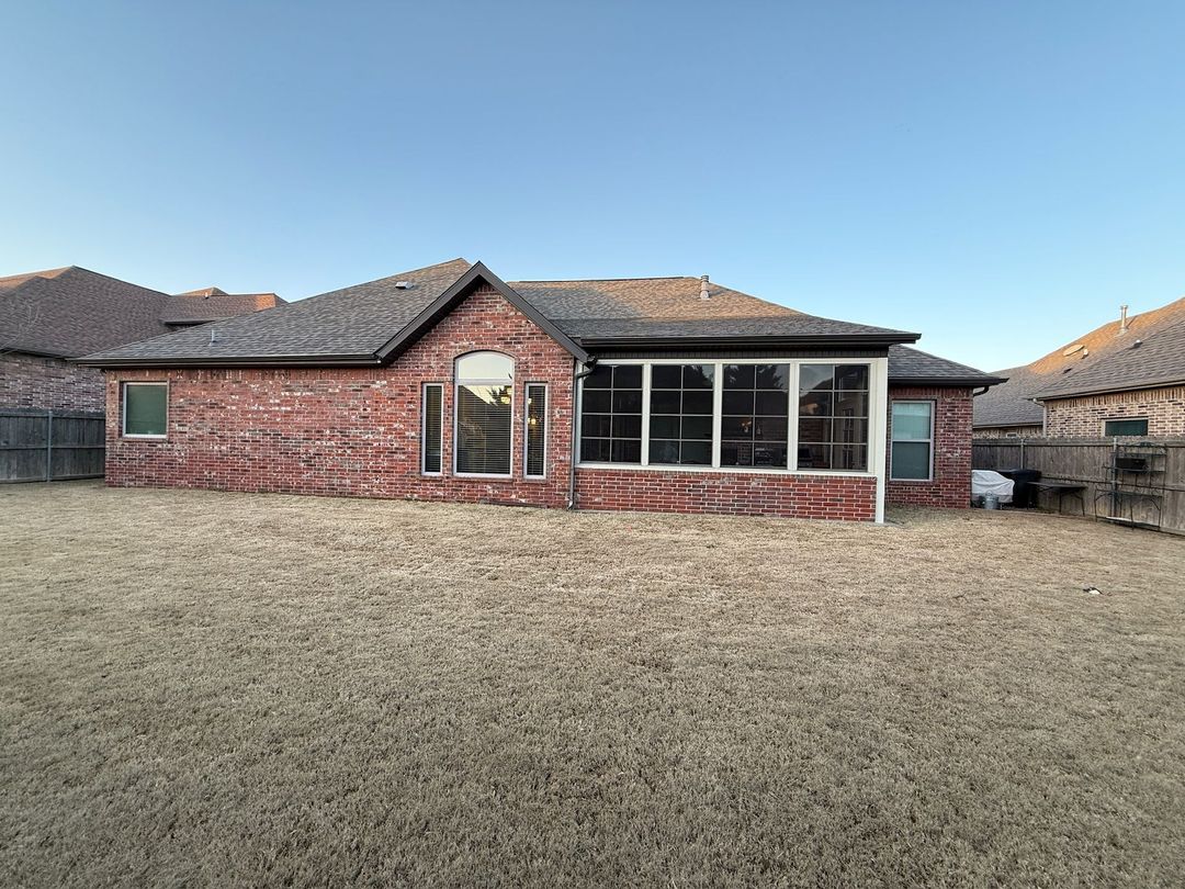 Single-story red brick house with a covered patio and large grassy yard under a clear sky