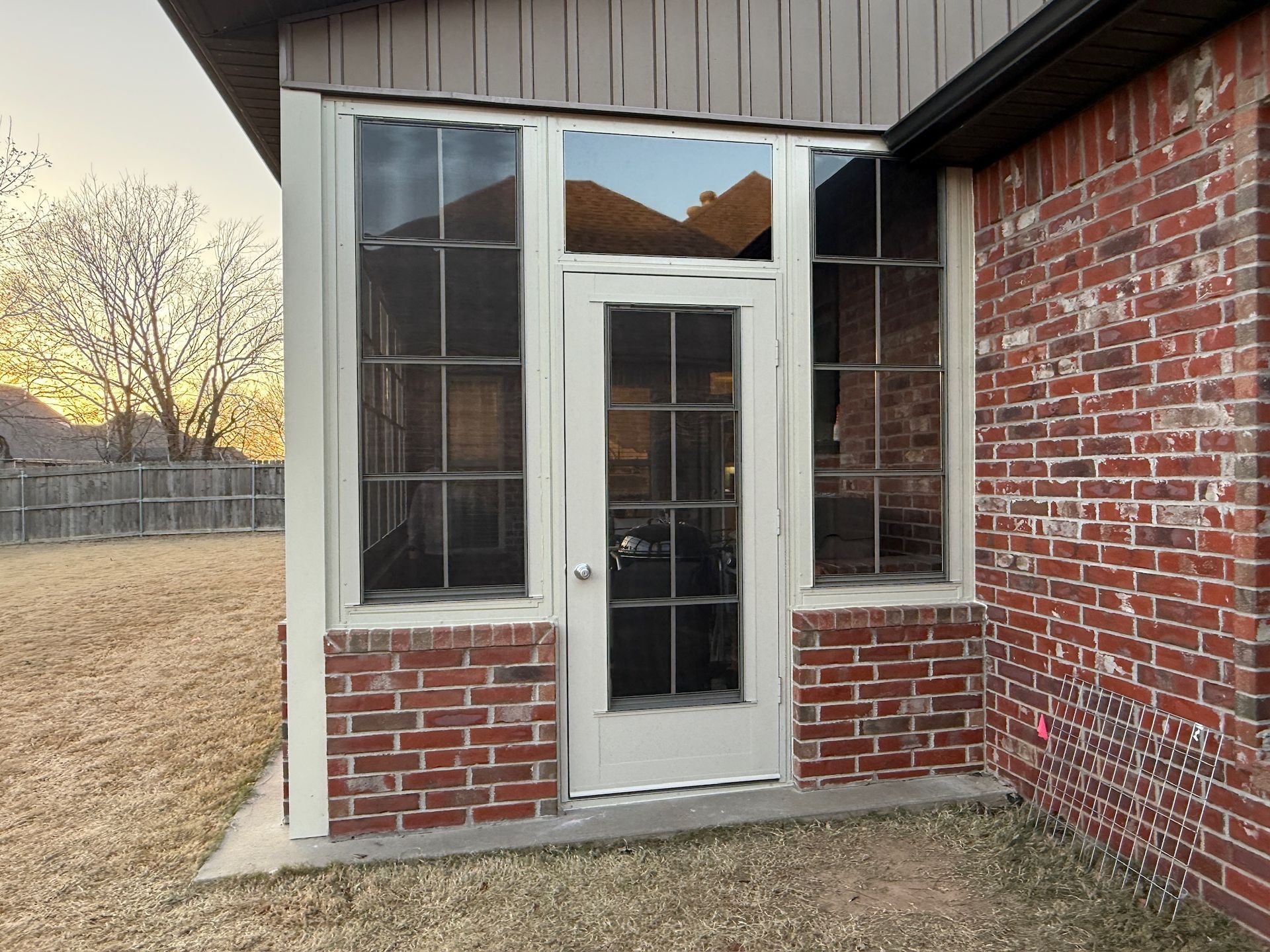 Brick house exterior with a white-framed glass door and windows under a brown roof overhang