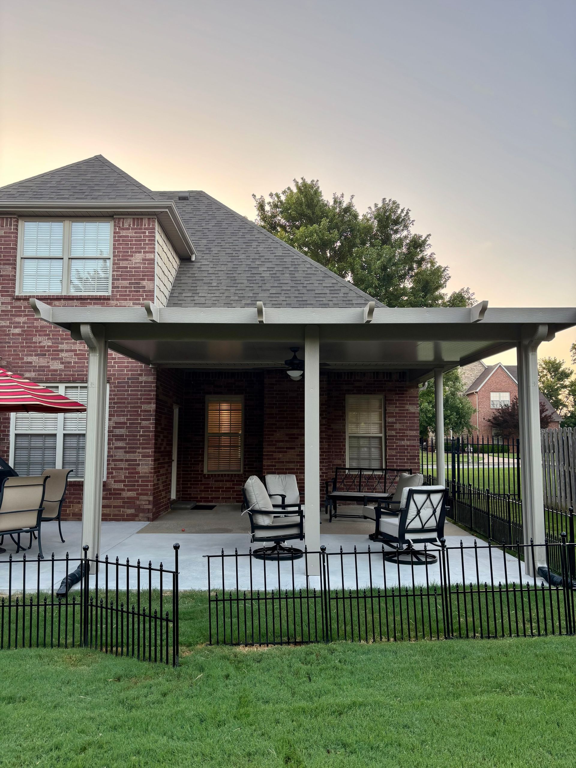 Brick house porch with black chairs, covered patio, and a small fenced yard at sunset