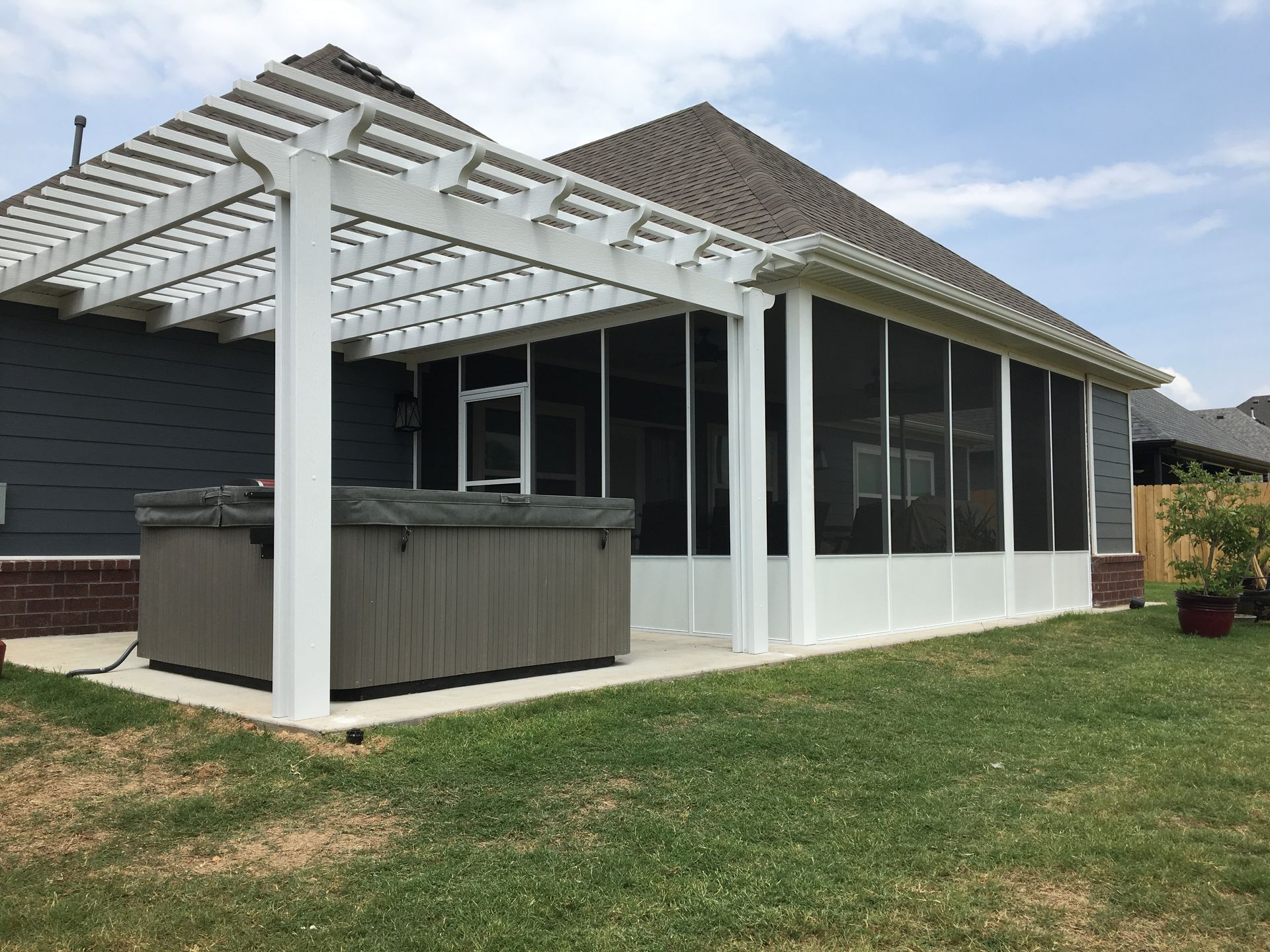Backyard patio with white pergola, screened enclosure, and hot tub beside a house