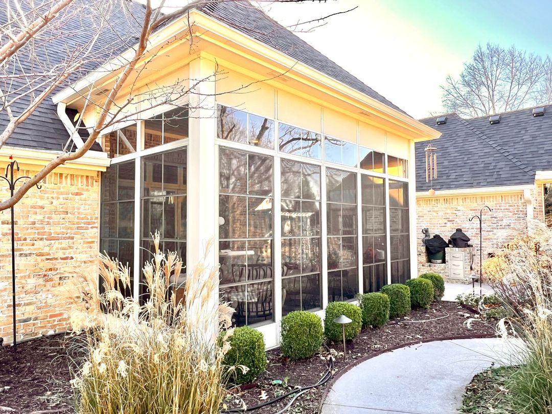 Sunlit screened porch with glass walls, brick exterior, and curved stone walkway