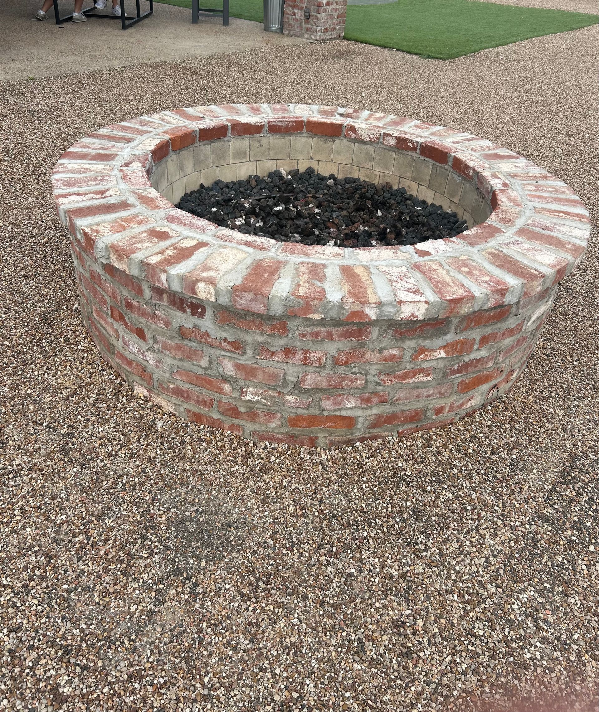 Round brick fire pit filled with black stones, set in a gravel-covered outdoor area