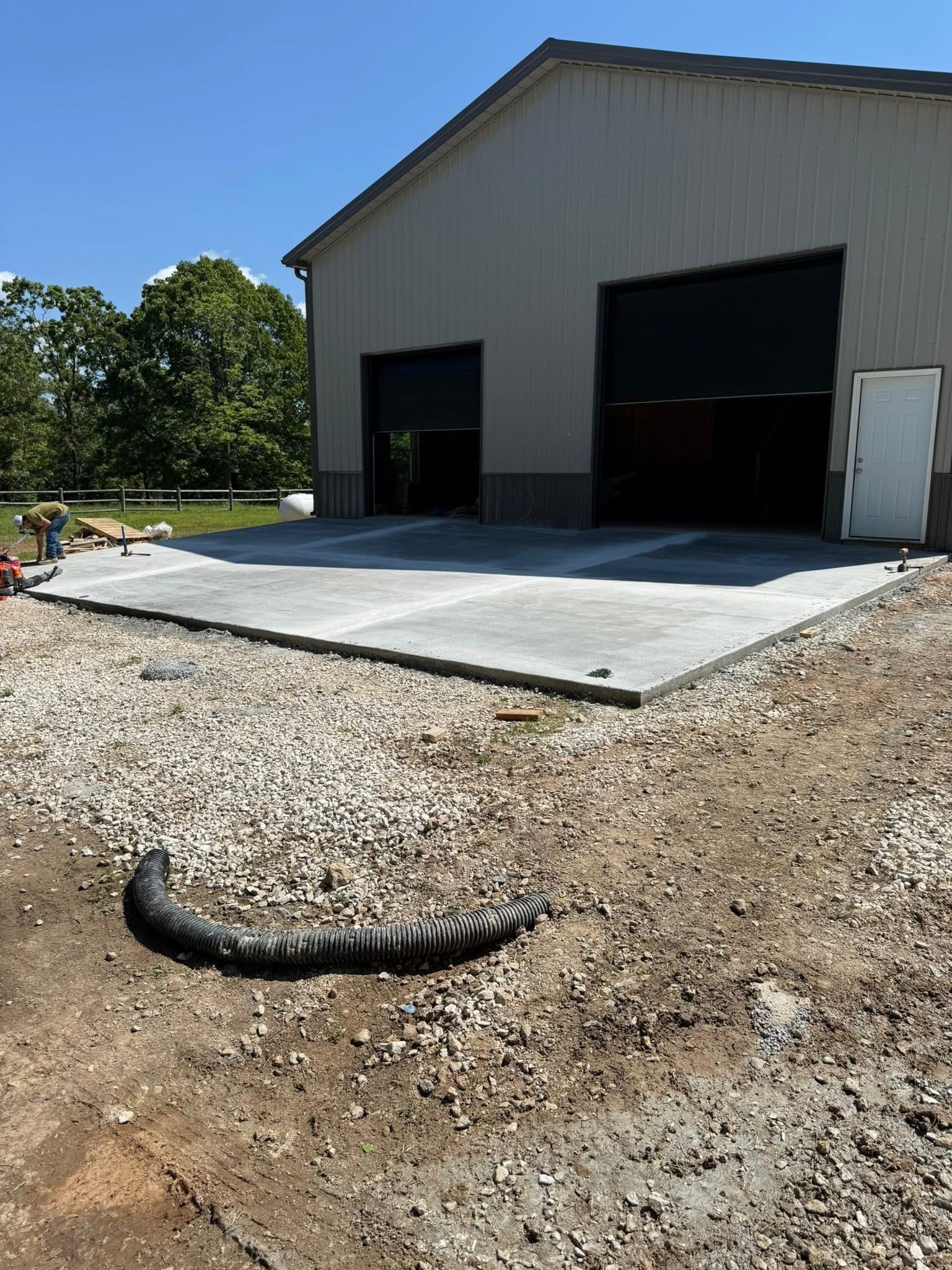 Gravel lot beside a metal warehouse with large open bay doors and a concrete loading pad