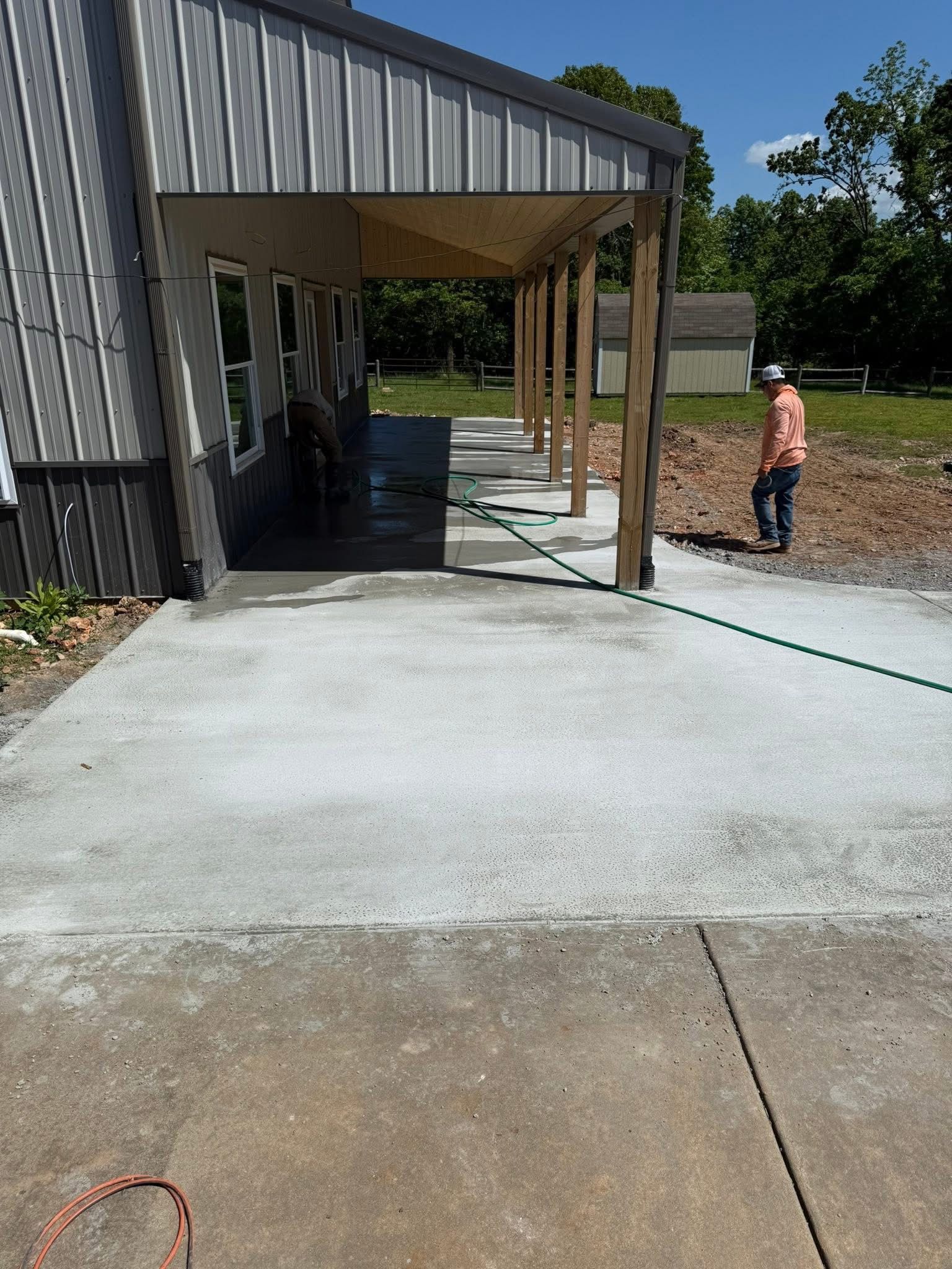 Concrete walkway beside a metal building under construction, with a person in orange on the right.