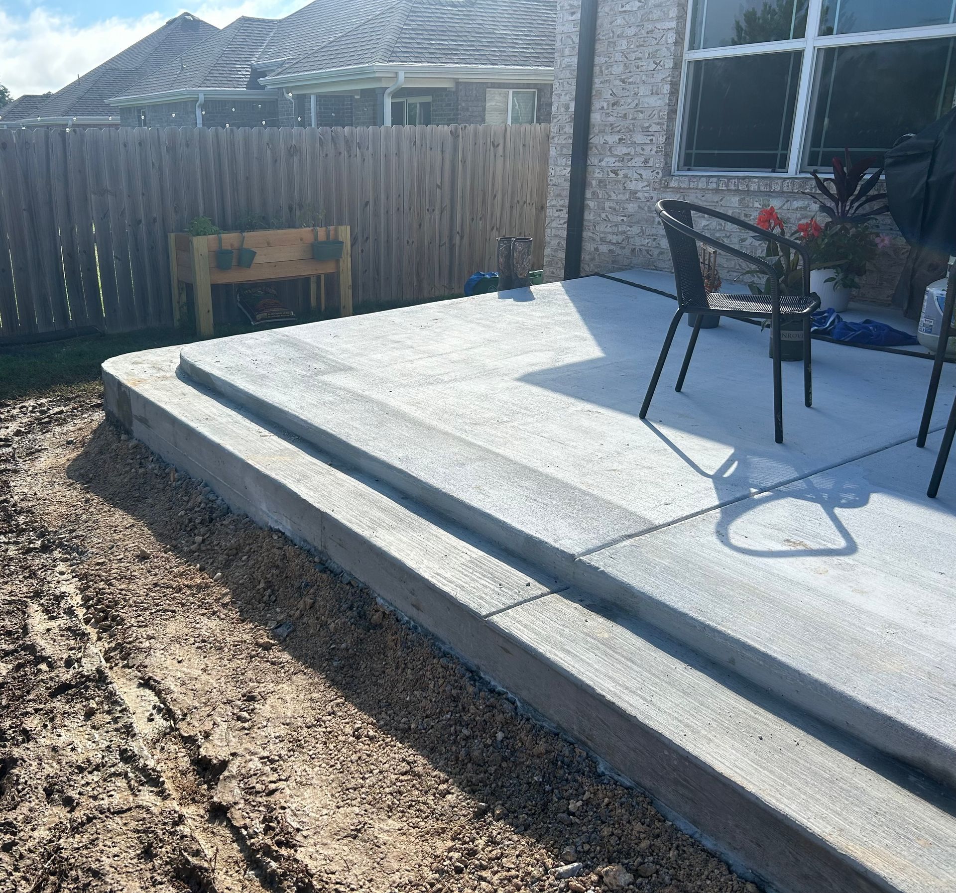 Backyard concrete patio with steps, a chair, and a wooden fence beside a house